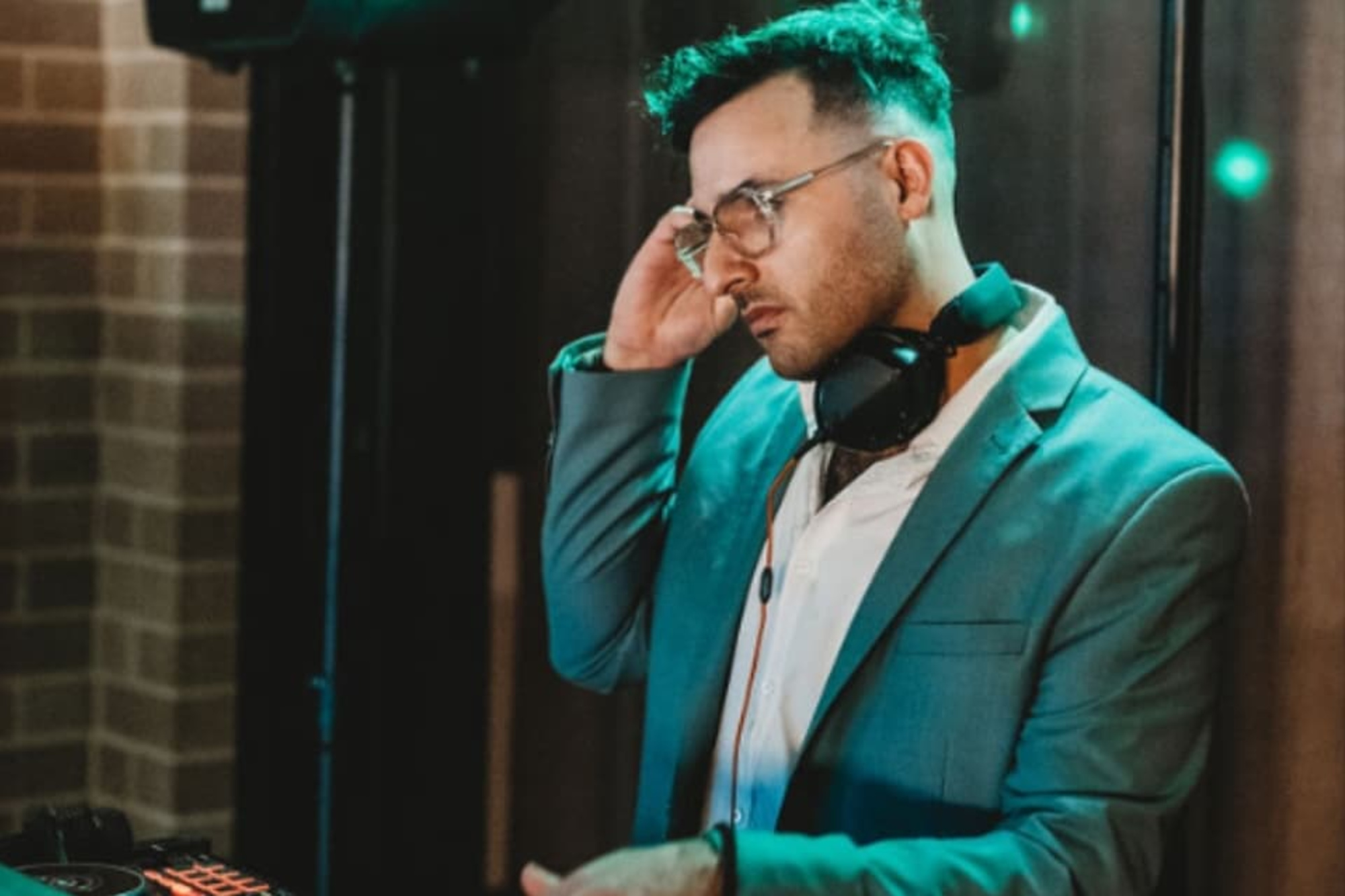 Wedding DJ in a suit mixing music at a reception with colorful lights in the background.