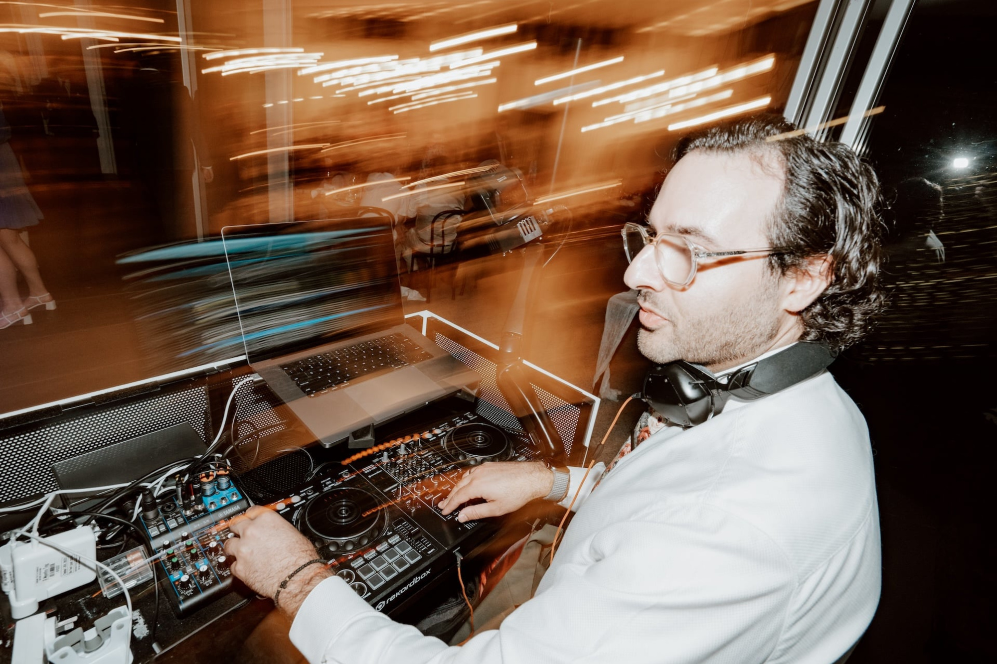 Wedding DJ mixing music at a reception with blurred warm lights in the background.