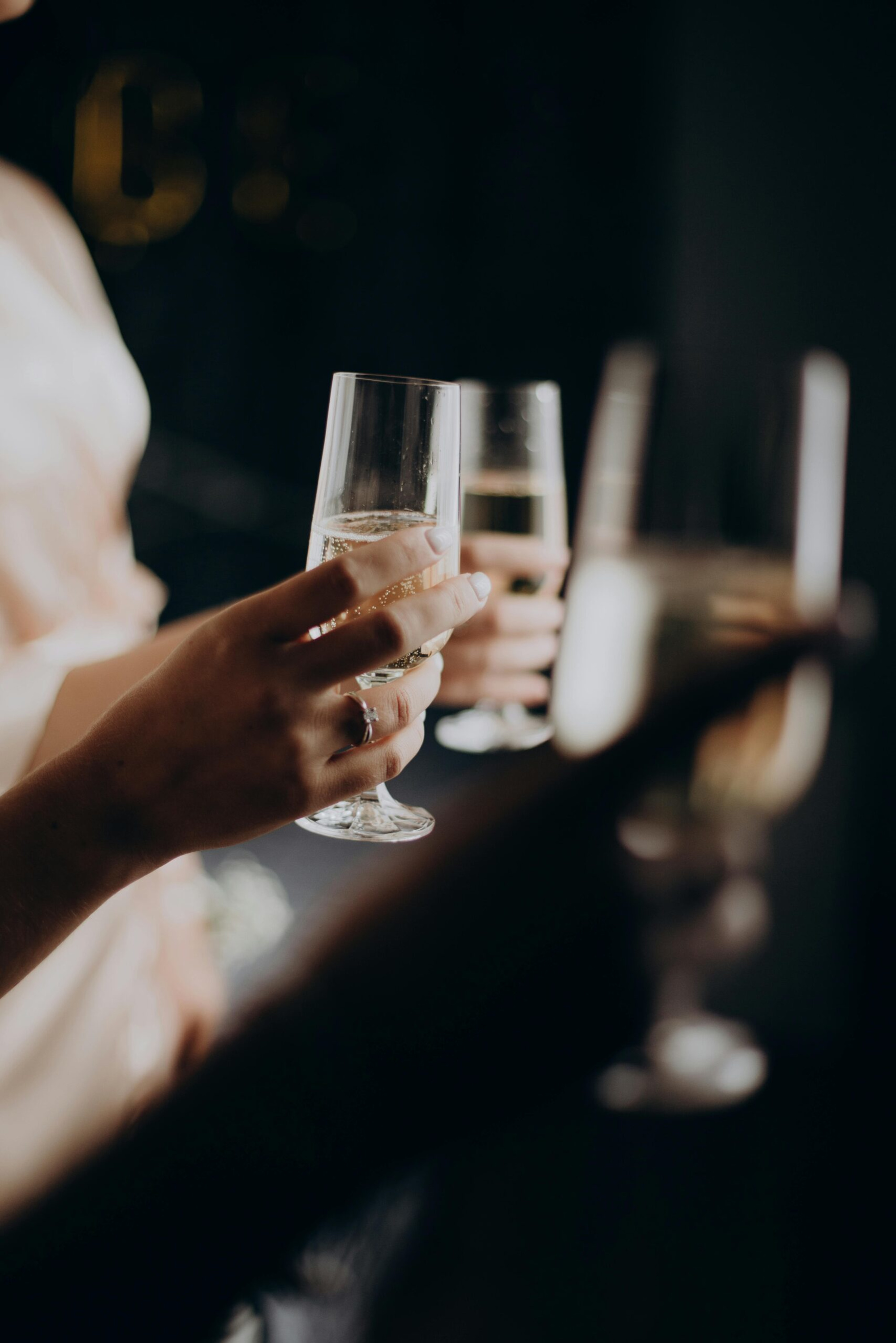 Close-up of guests raising champagne flutes in a dimly lit wedding toast.