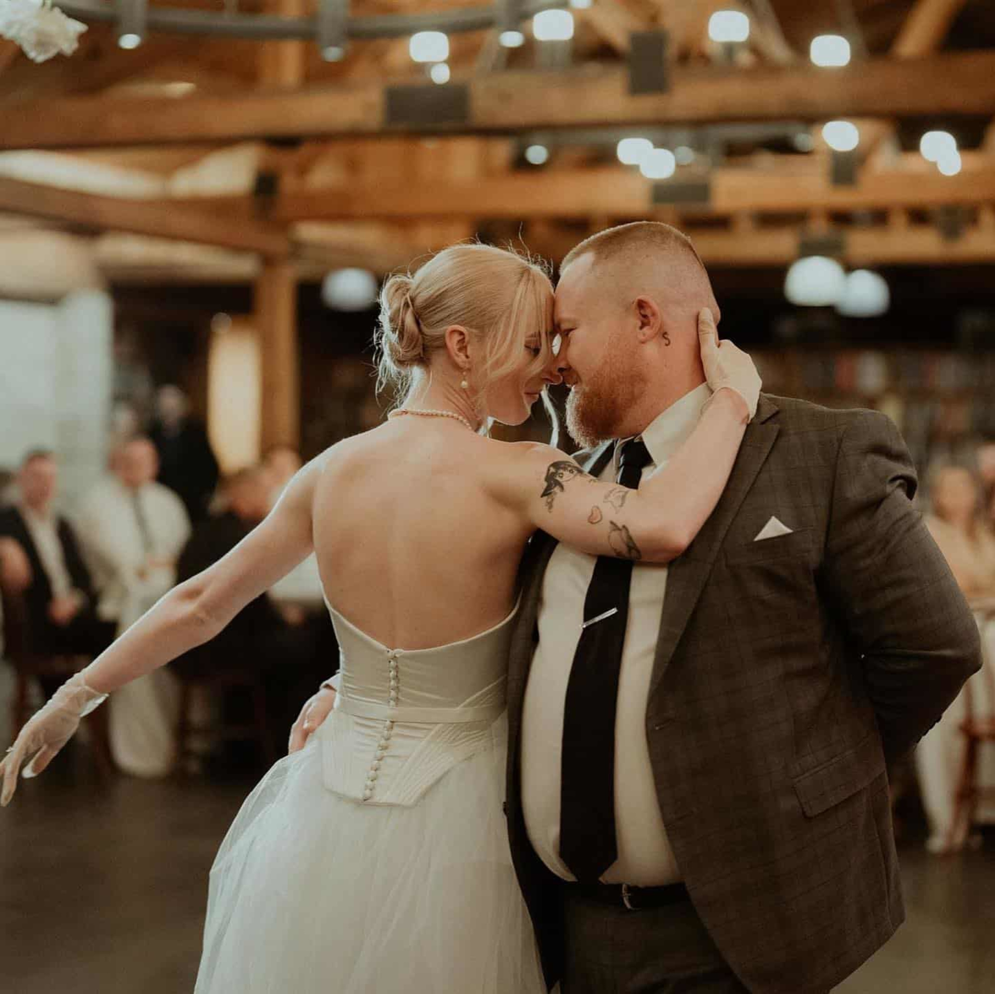 Bride and groom share an intimate first dance in a warm, rustic indoor reception space.