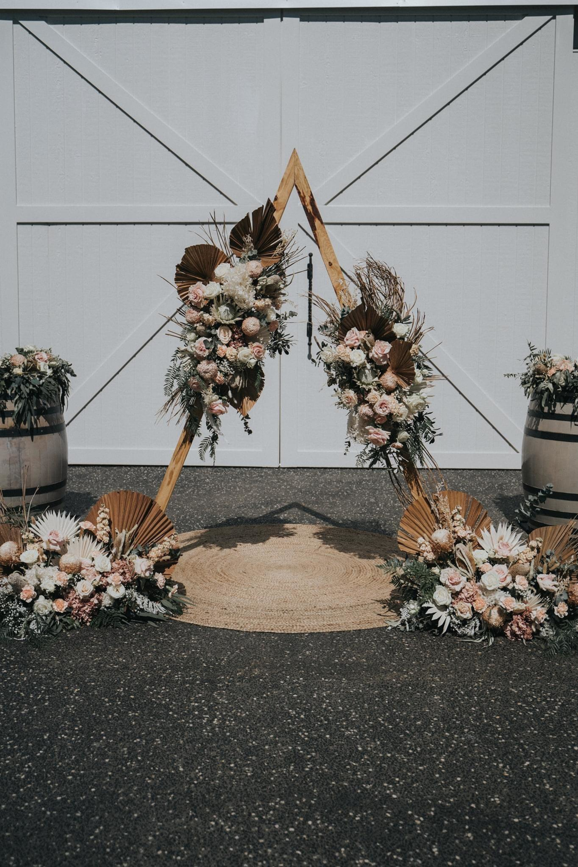 Boho wedding ceremony arch with dried palms and blush florals in front of white barn doors.