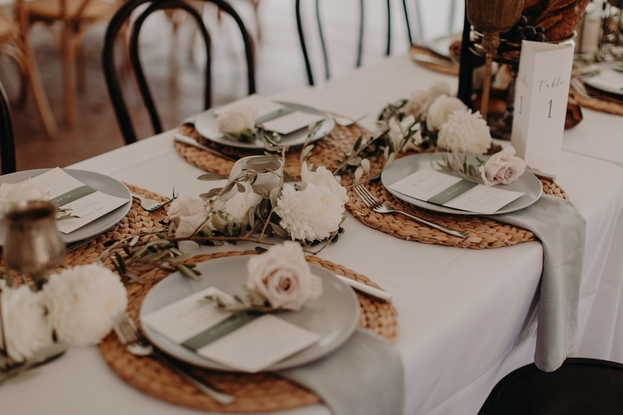Elegant wedding reception table with woven placemats, neutral florals, and simple place settings.
