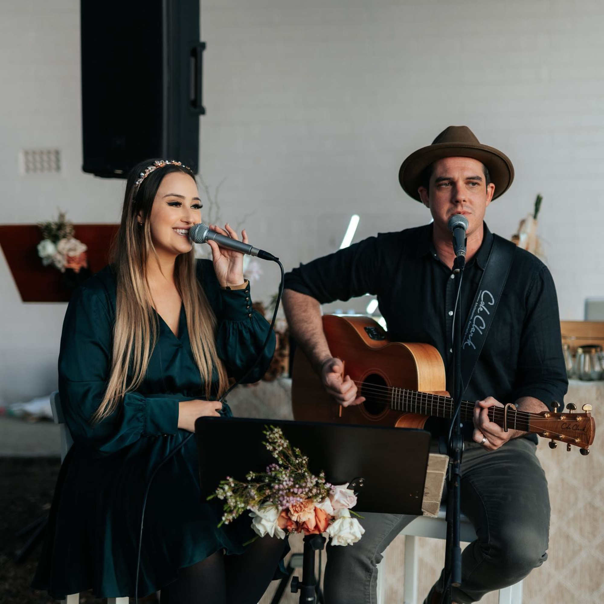Acoustic duo performing live wedding music with microphone and guitar beside floral decor.