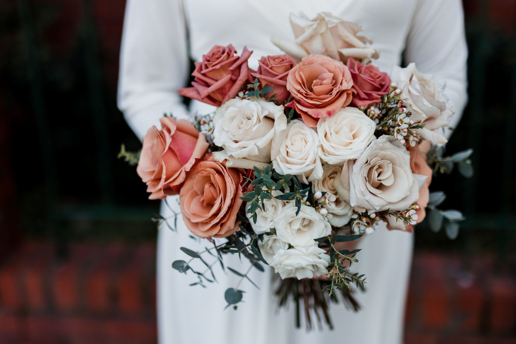 Close-up of a bride holding a rose-filled wedding bouquet in warm peach and cream tones.