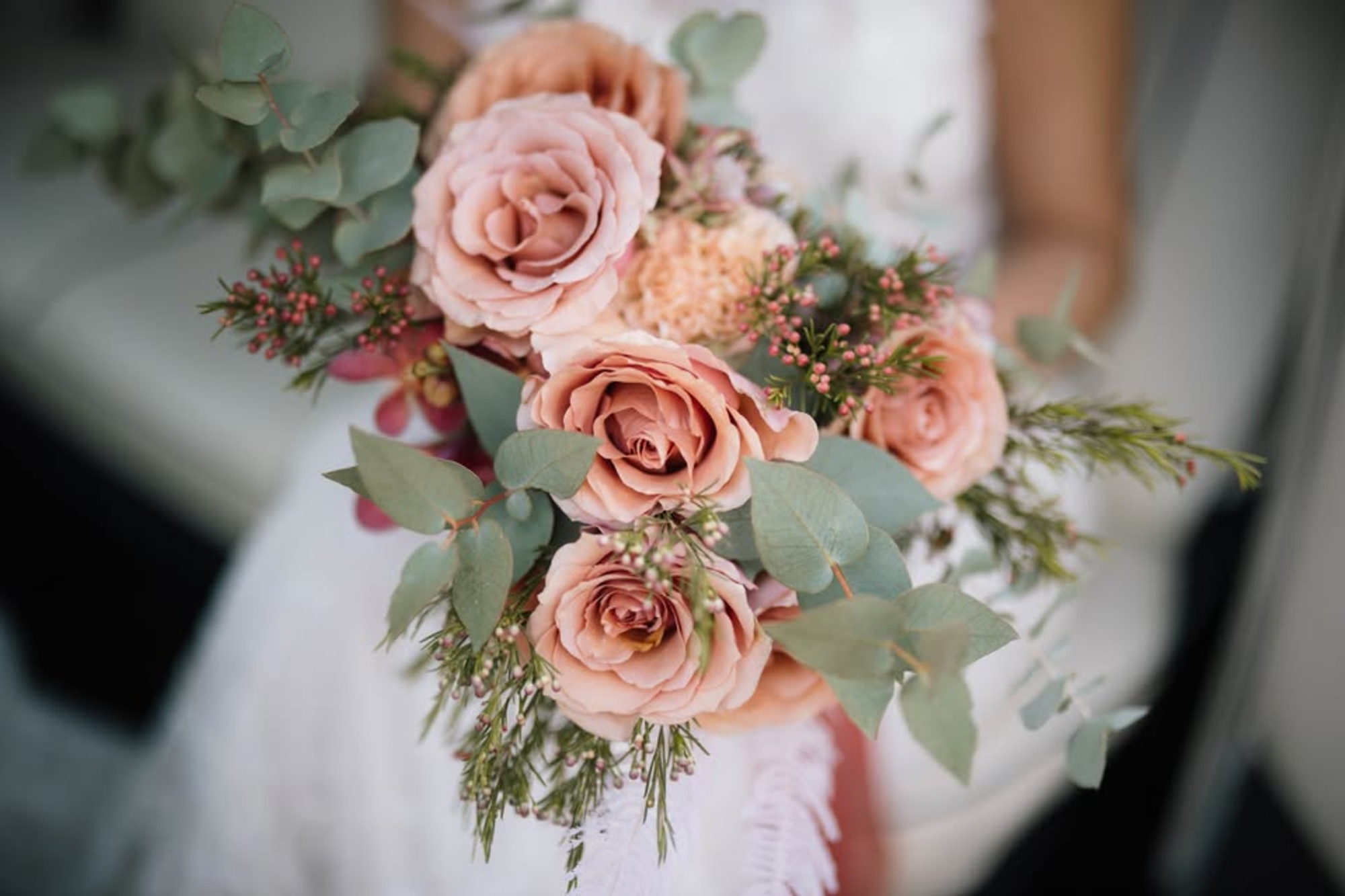 Close-up of a bridal bouquet with blush roses, eucalyptus, and greenery held by a bride.