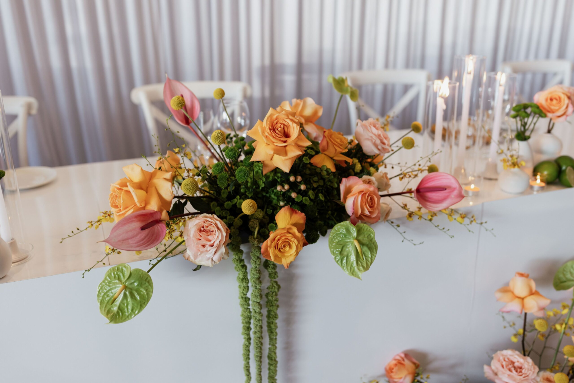 Elegant wedding sweetheart table with peach and pink floral arrangement and candles on a white backdrop.
