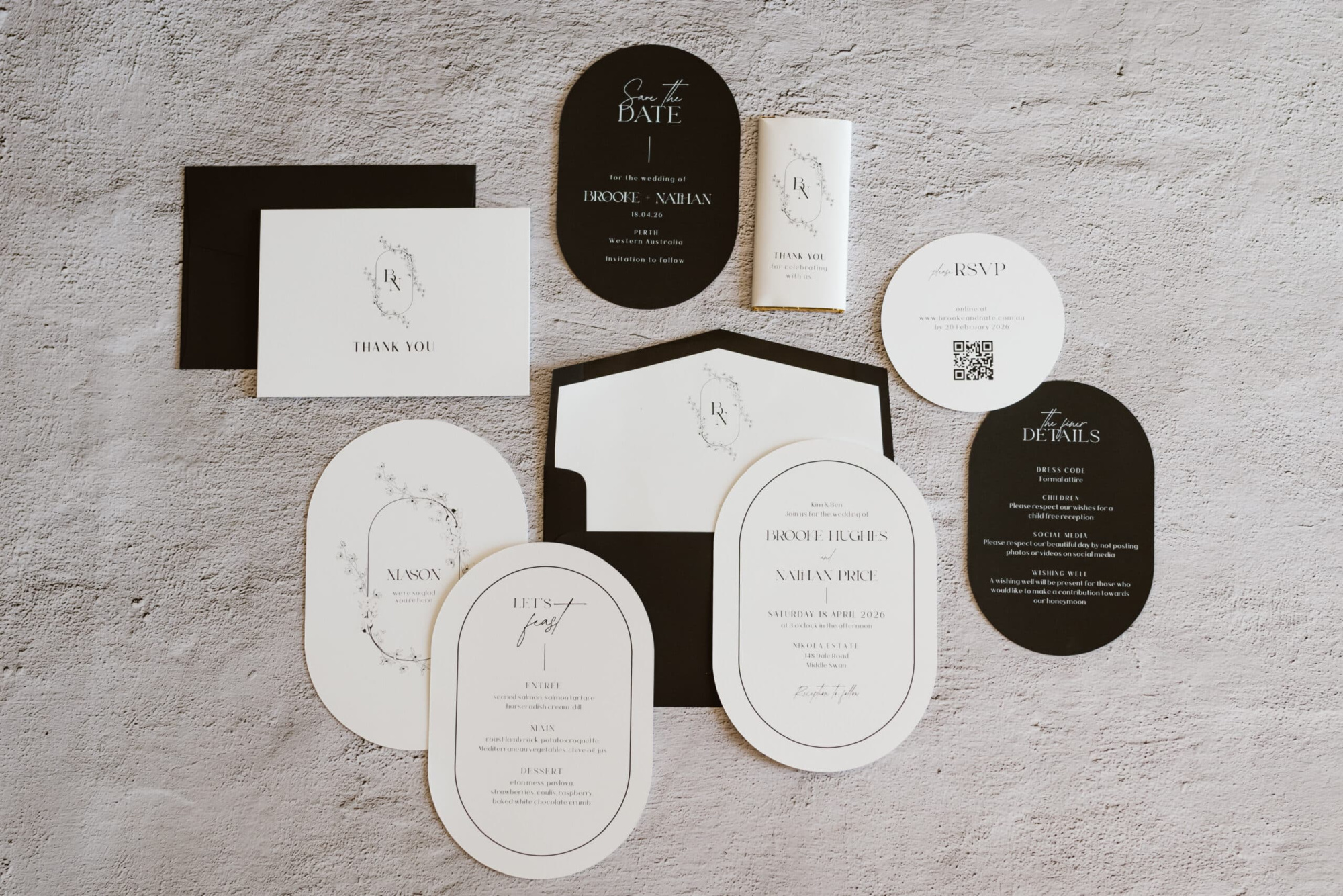 Flatlay of a modern black and white wedding invitation suite with various cards and envelopes on a textured surface.