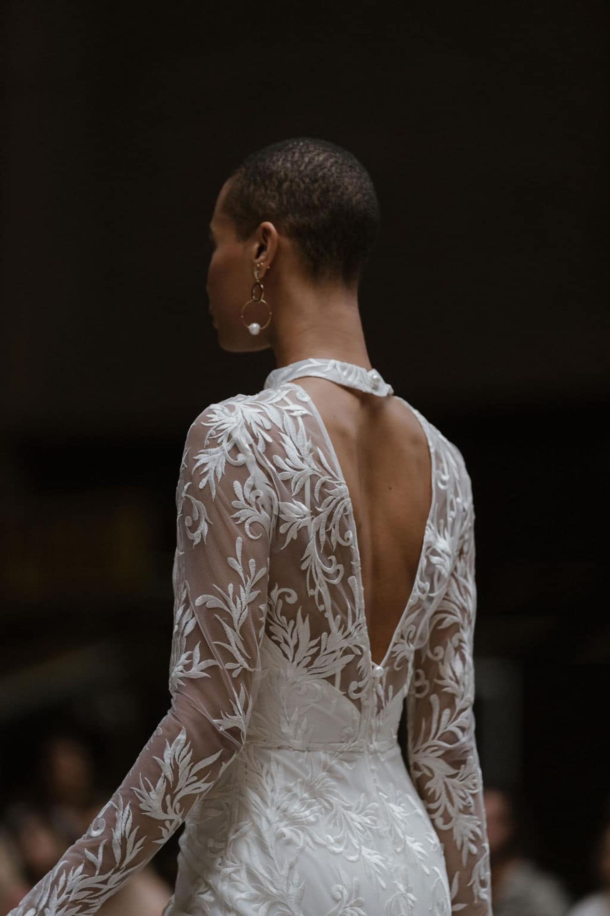 Bride wearing a long-sleeve lace open-back wedding gown with floral embroidery.