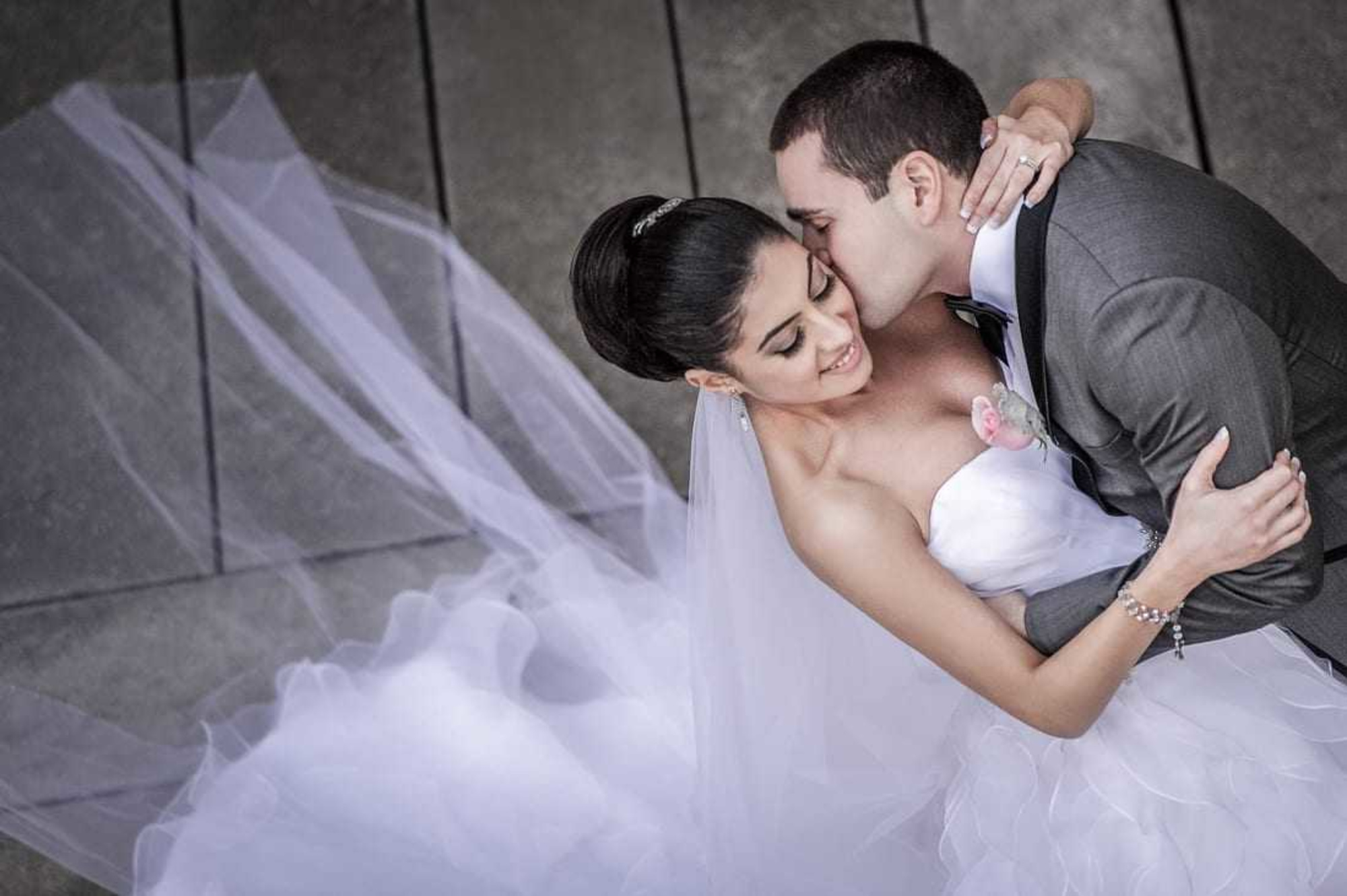 Bride and groom embrace lovingly as her flowing veil and dress spread out around them.