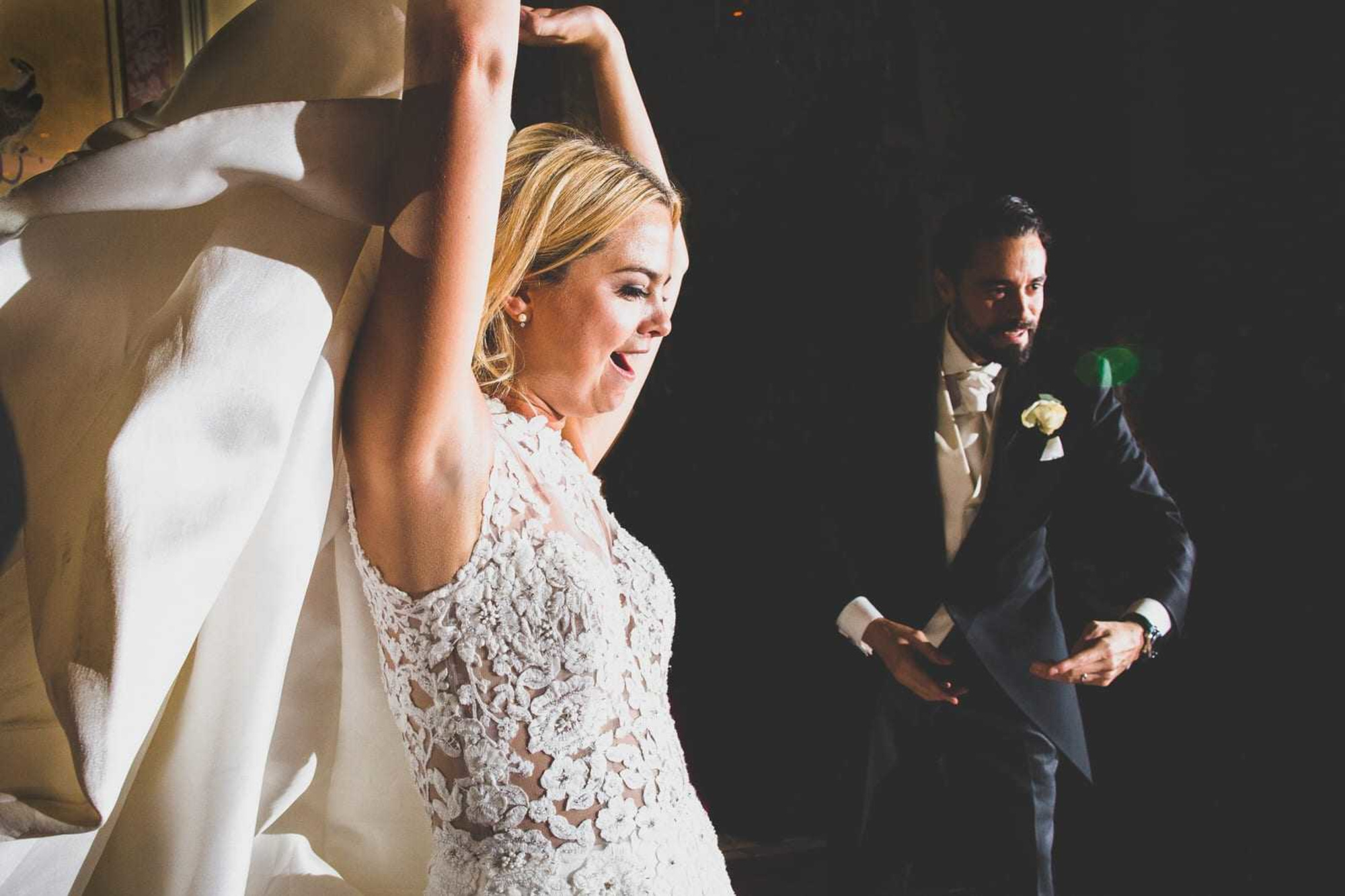 Candid moment of a bride lifting her arms and smiling while dancing with the groom at their wedding reception.