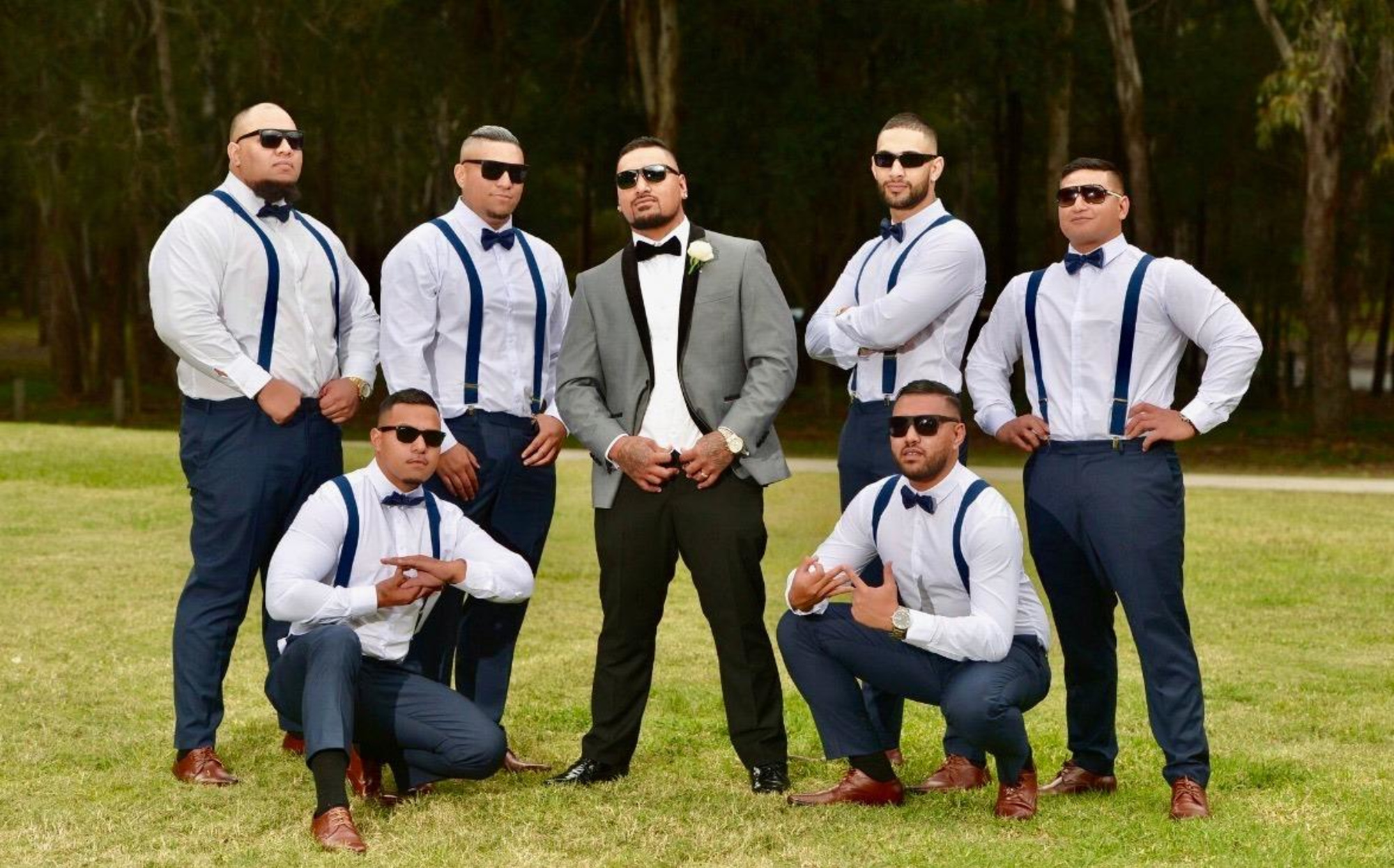 Groom and groomsmen in coordinated navy and white outfits posing together in an outdoor setting.