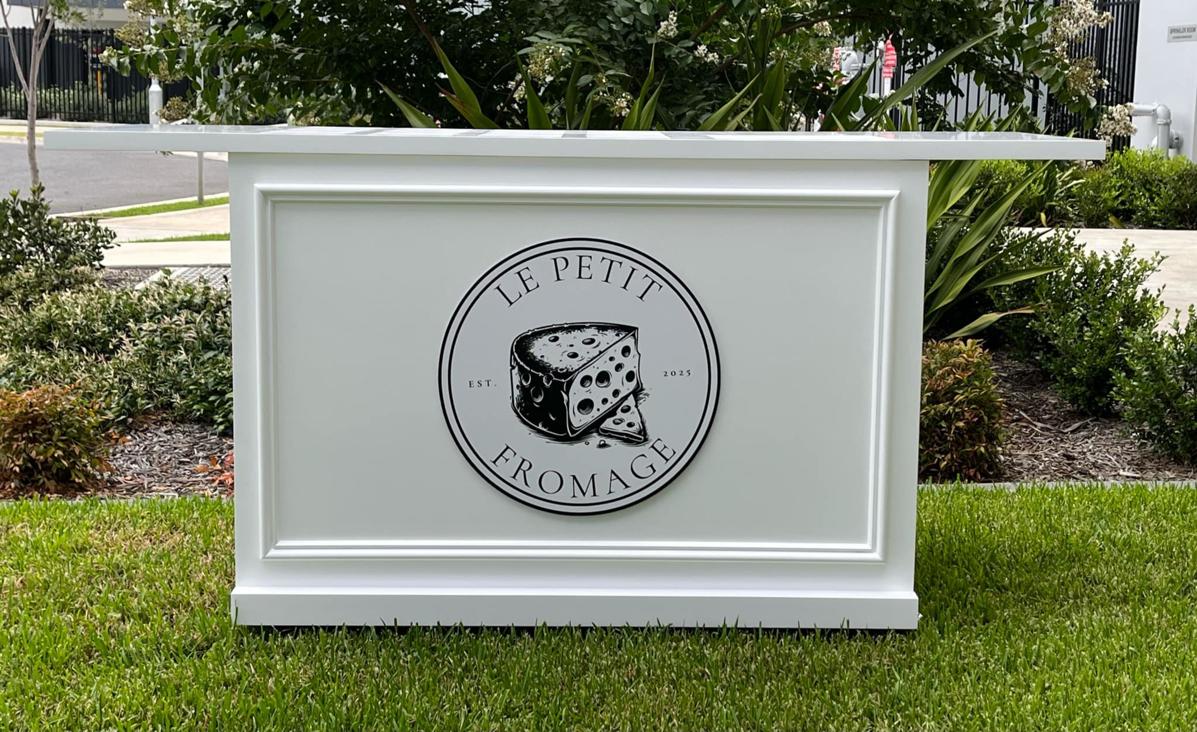 White Le Petit Fromage catering bar with cheese logo set on green lawn outdoors.