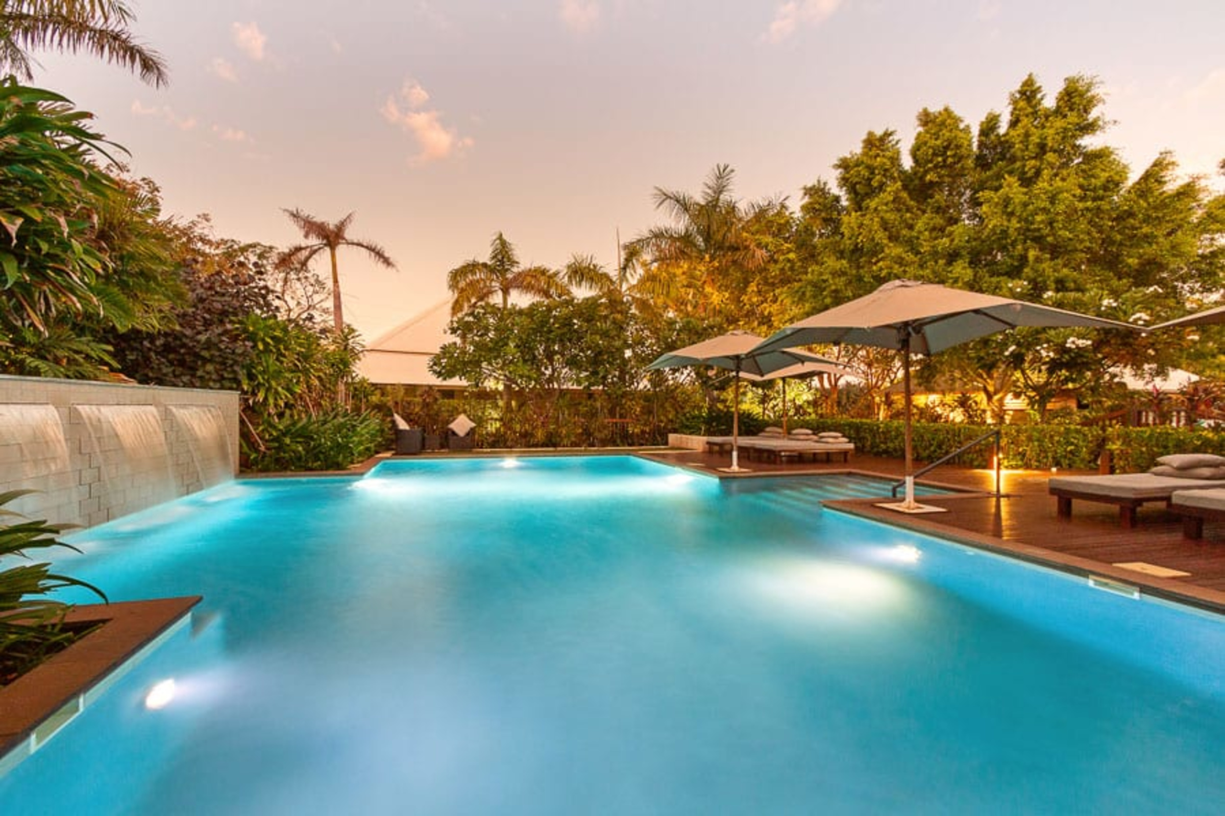 Sunset view of a tropical resort pool with lounge chairs and umbrellas for an outdoor wedding venue.
