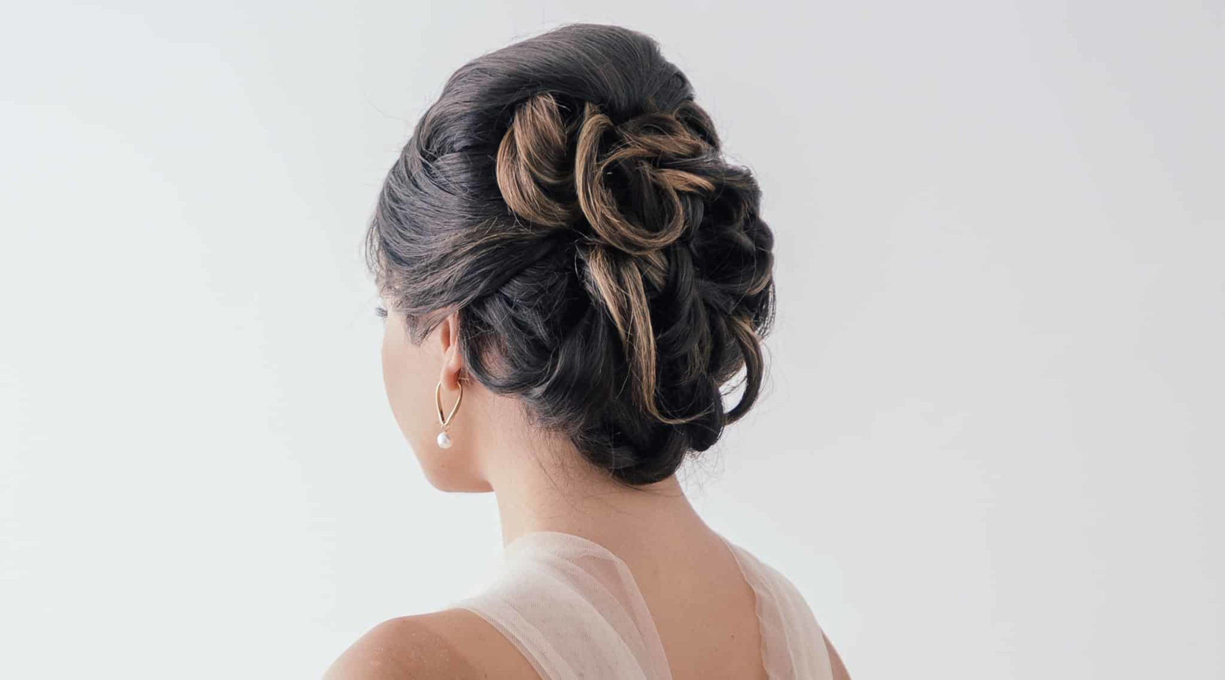 Bride shown from behind with an elegant curled updo and pearl earring against a light background.