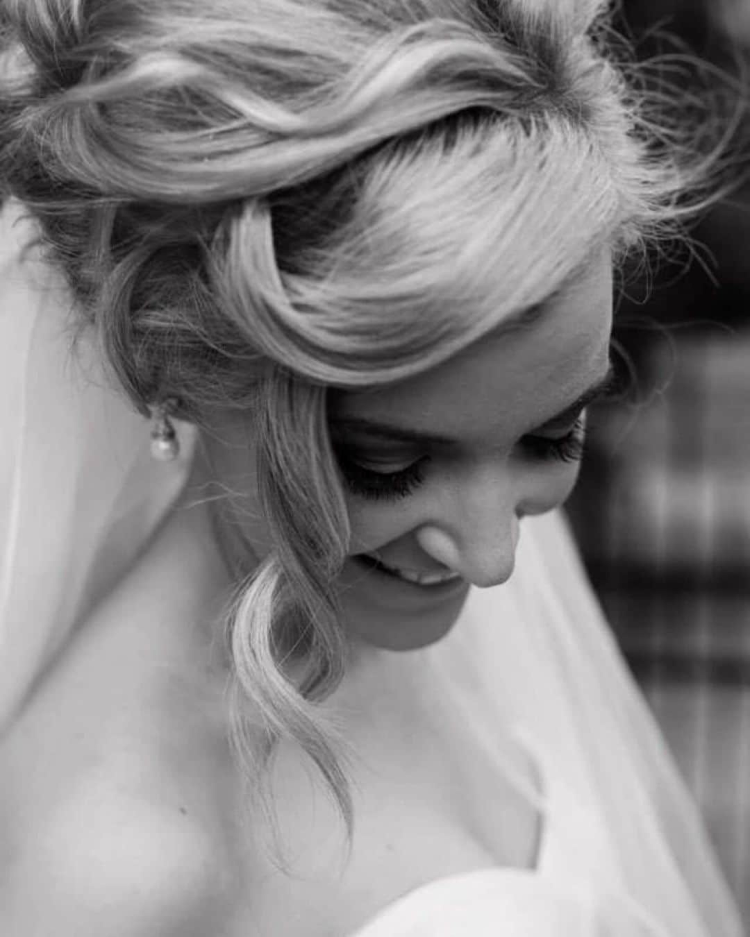 Black and white close-up of a smiling bride with styled hair, veil, and soft makeup looking down.