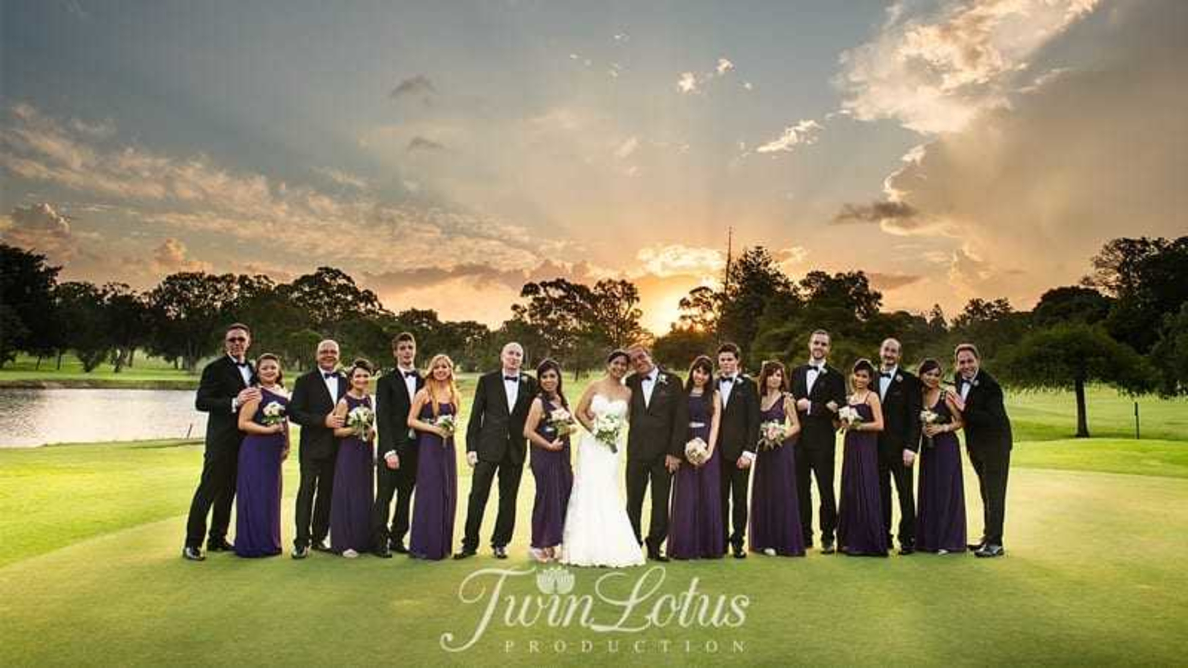 Wedding party poses with the couple on a golf course at sunset with dramatic sky in the background.