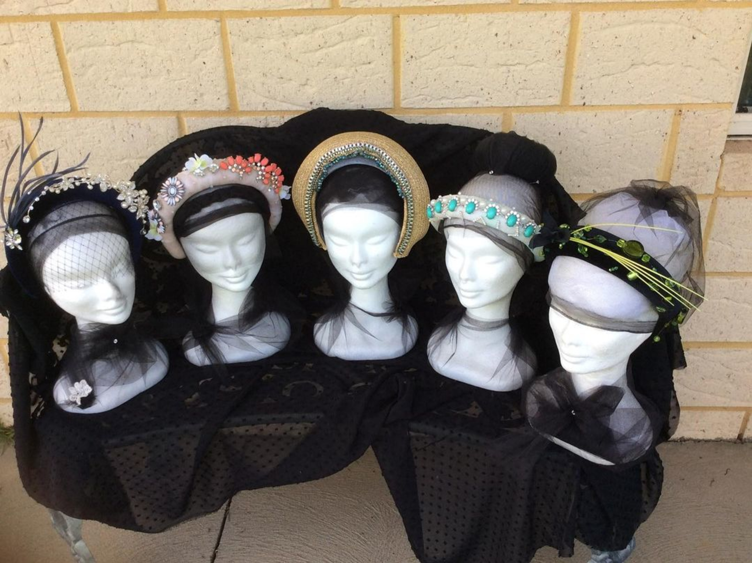 Display of ornate bridal headbands and fascinators on mannequin heads draped in black tulle.