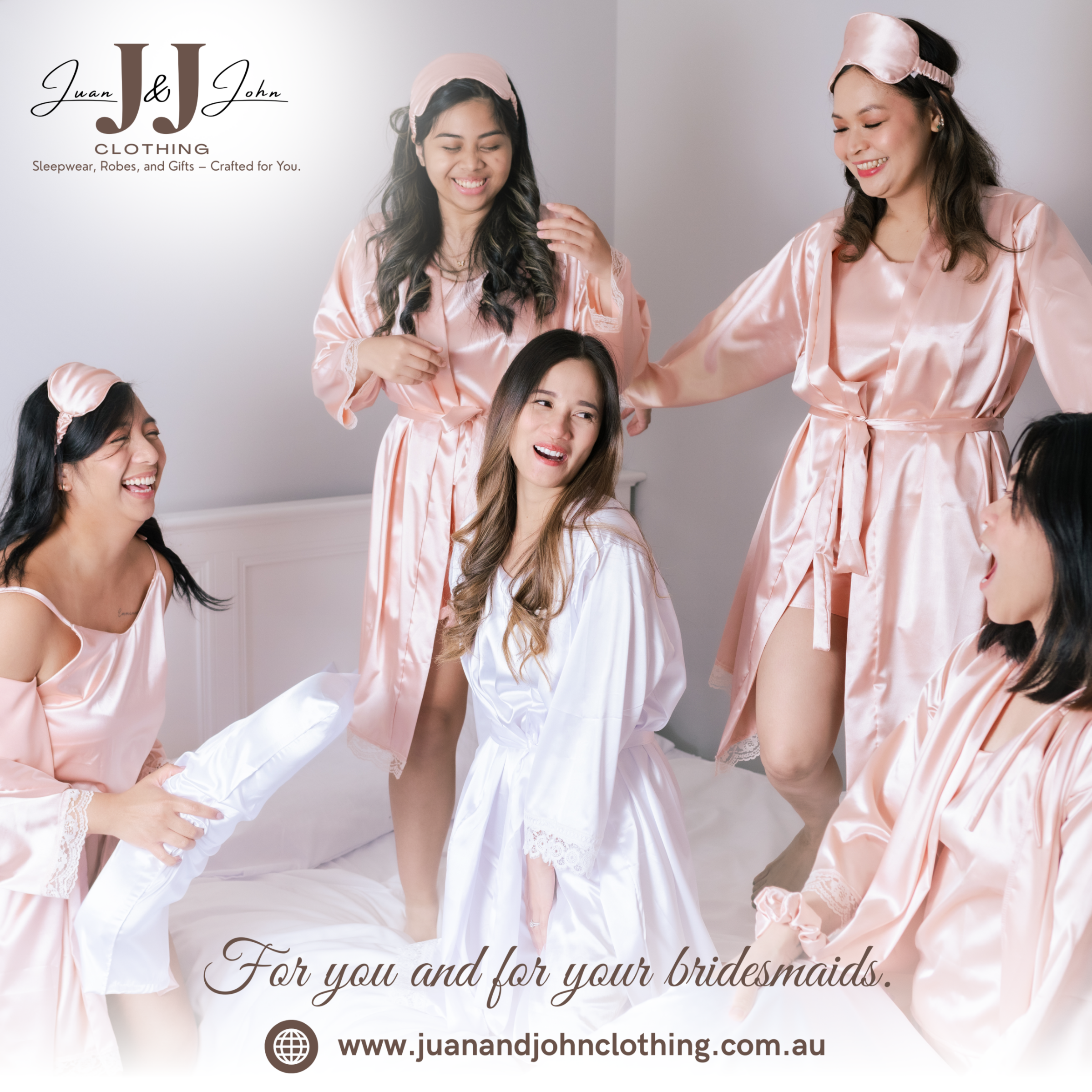 Bride and bridesmaids in satin robes laughing and getting ready together on a bed.