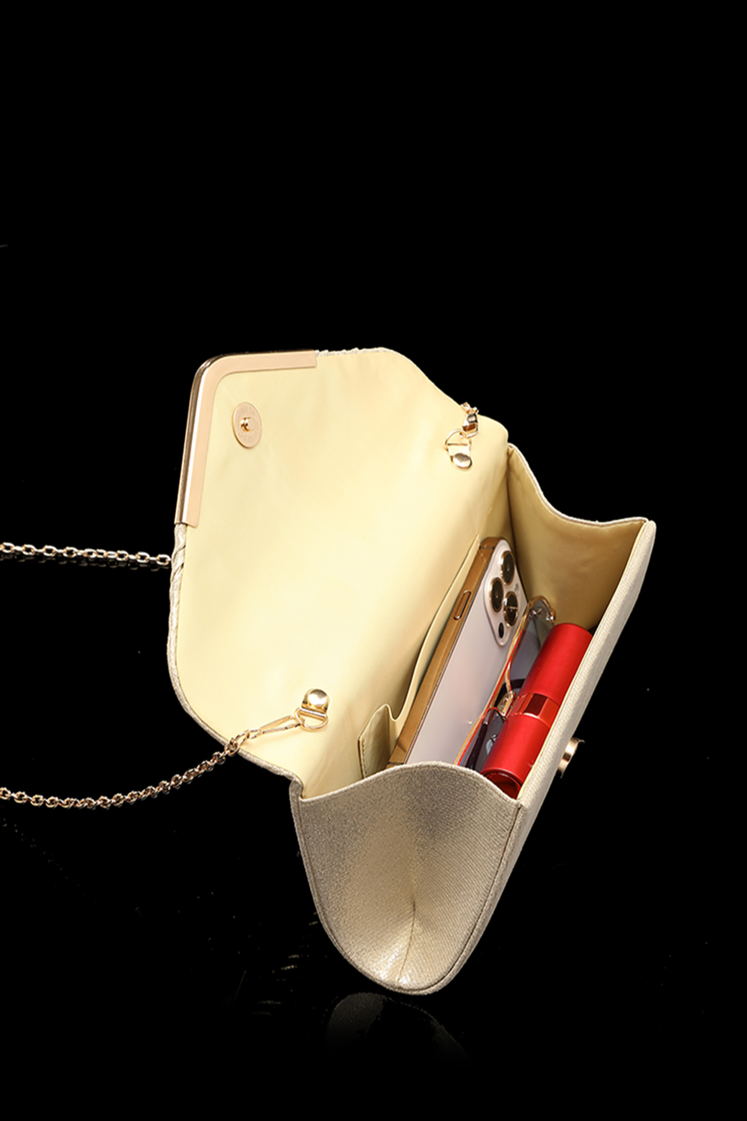 Open gold evening clutch with chain strap showing phone and lipstick inside on a black background.