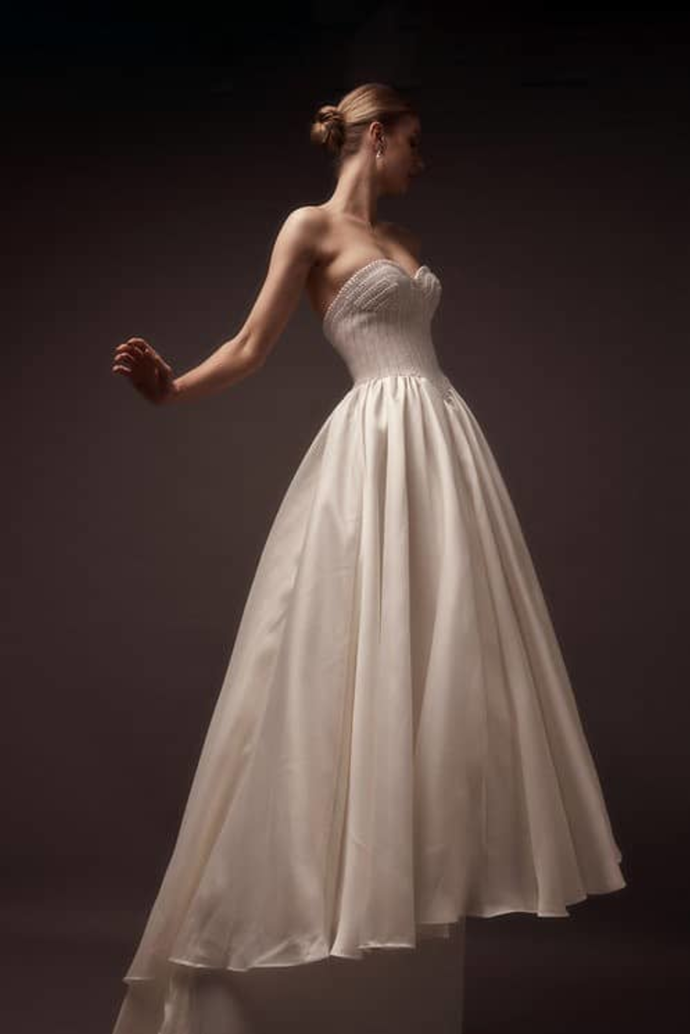 Bride wearing a strapless ivory ballgown wedding dress posed against a dark studio background.