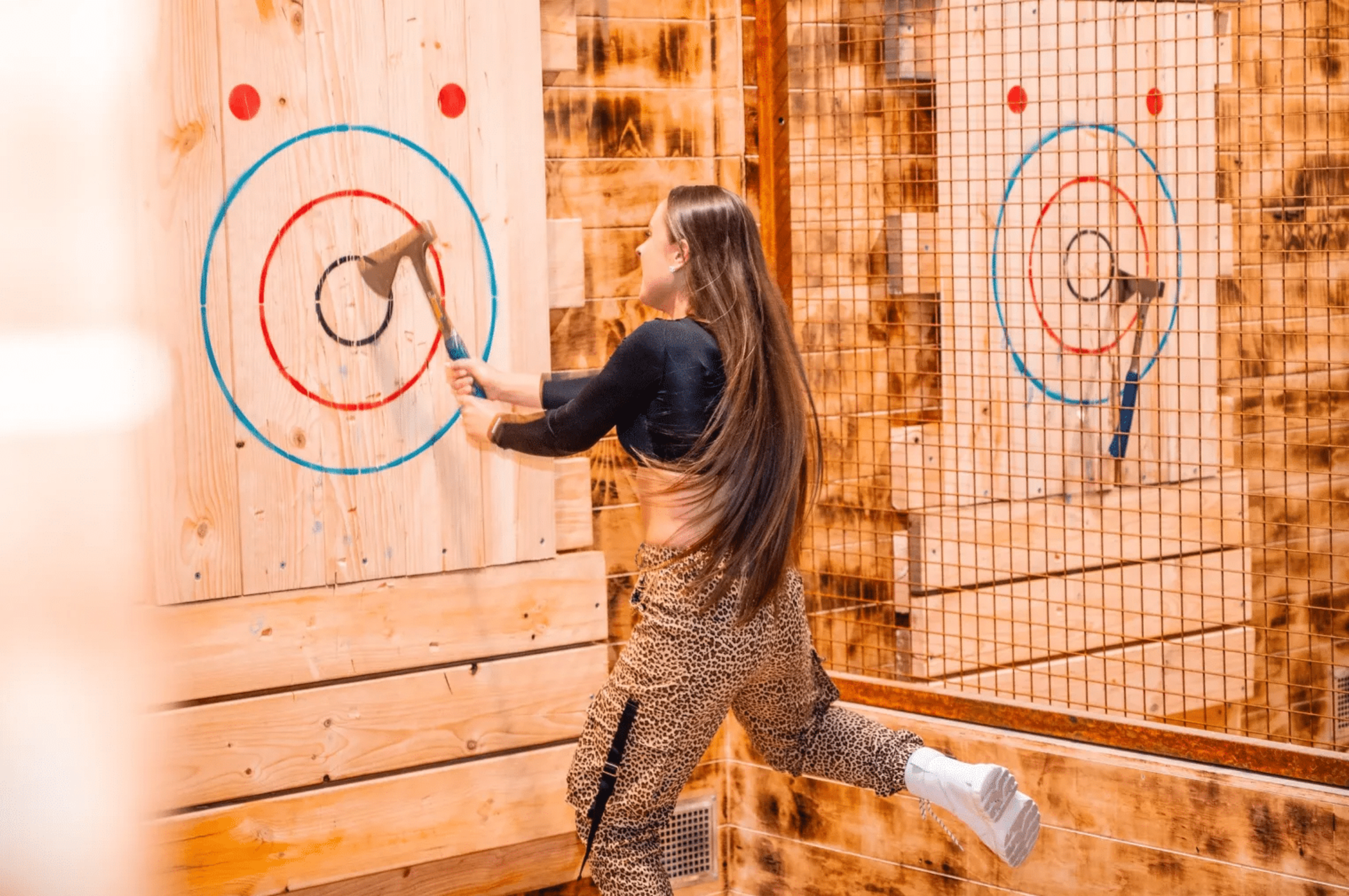 Woman throwing an axe at a wooden target inside an indoor axe-throwing venue.