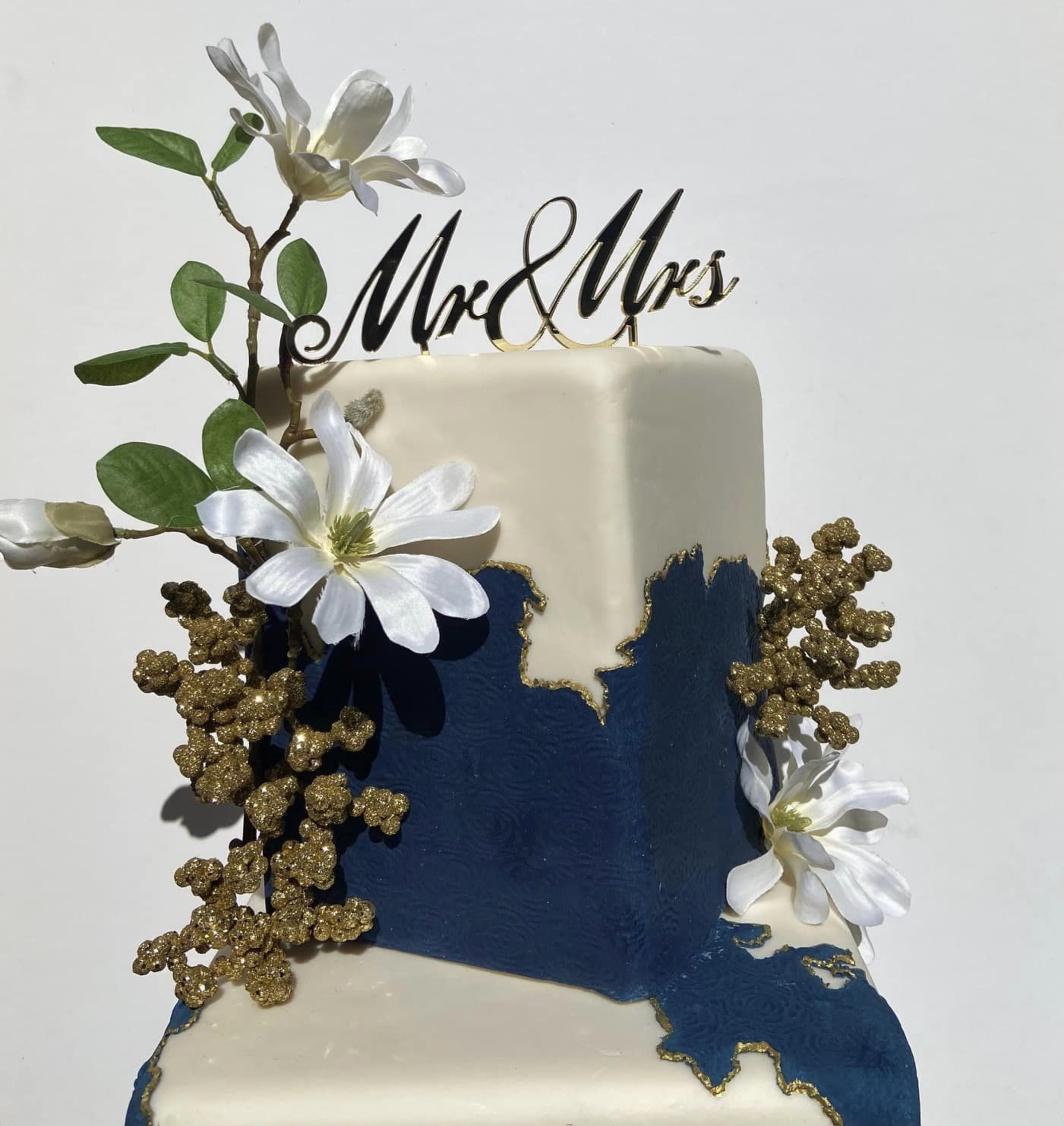 Two-tier navy and ivory wedding cake with gold details, white flowers, and a Mr & Mrs topper.