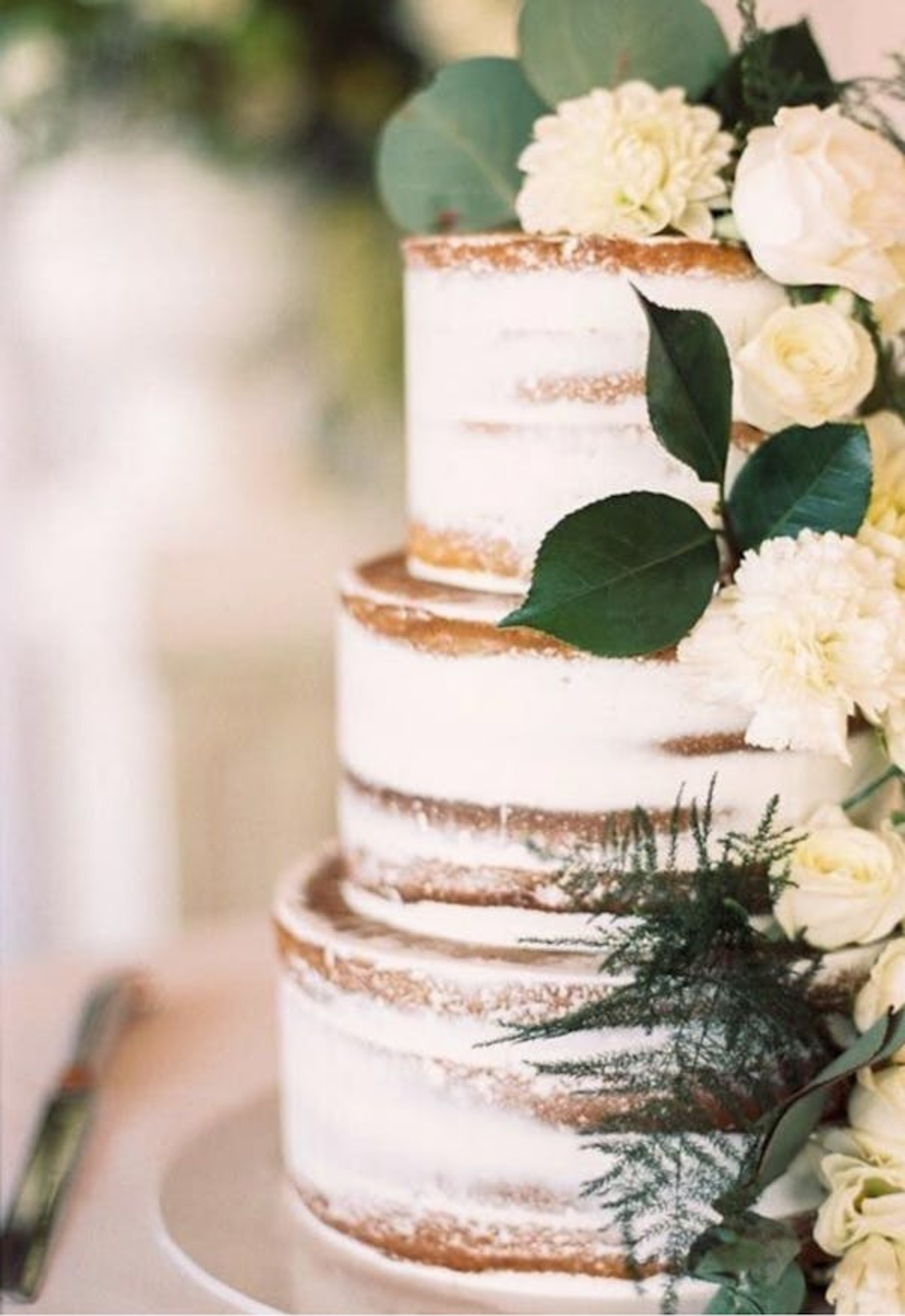 Three-tier semi-naked wedding cake decorated with white flowers and greenery.