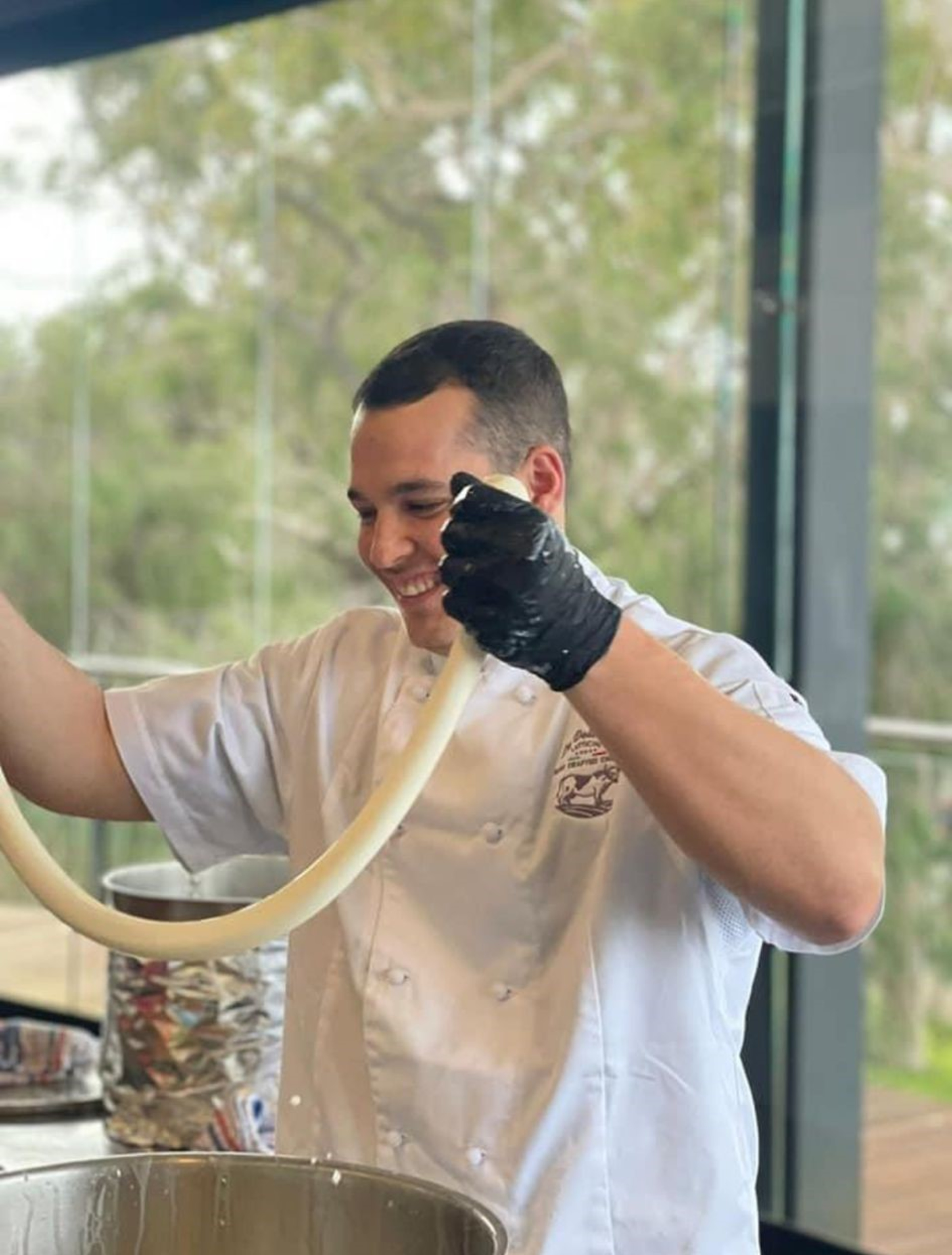 Smiling chef in a white uniform stretching dough or cheese at a live cooking station.