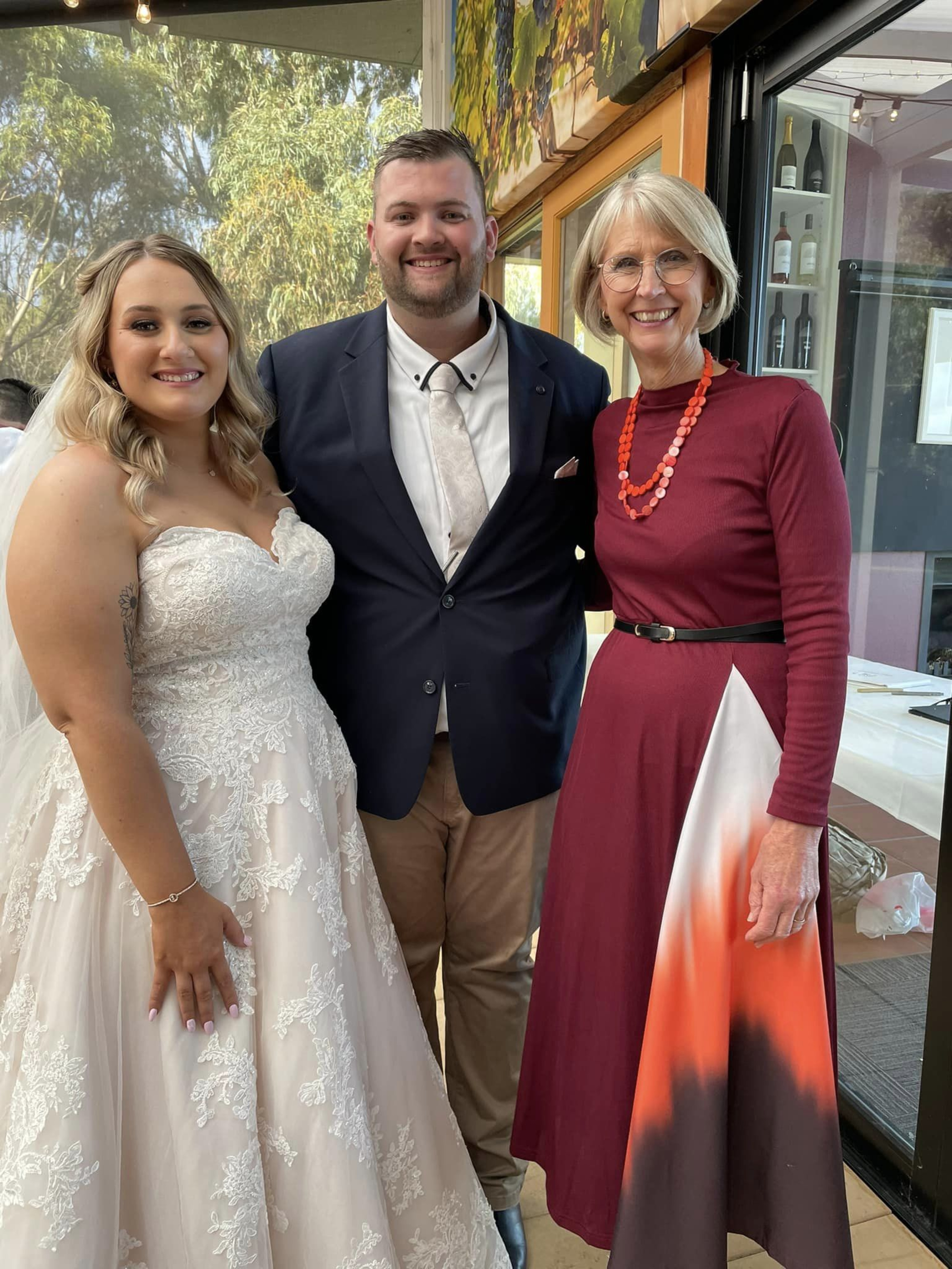 Bride and groom posing with an officiant at an indoor wedding reception.