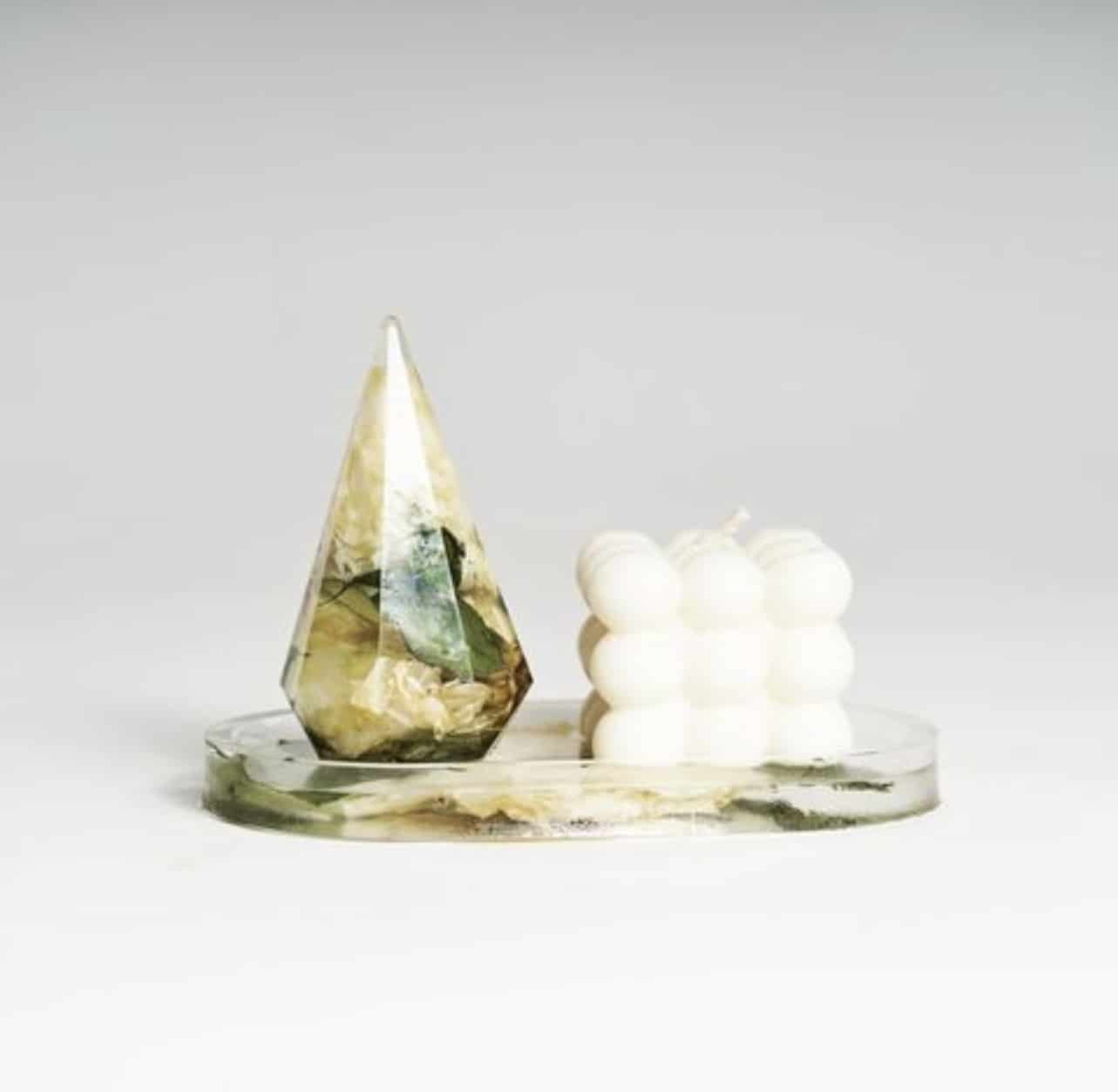 Modern geometric resin decor and sculptural white candle displayed on a round tray.