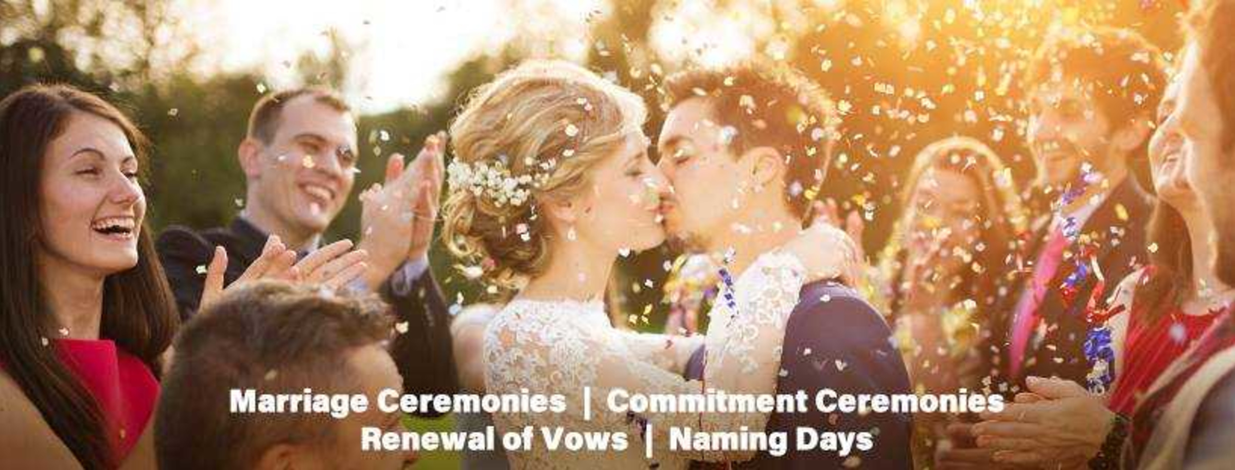 Bride and groom kiss under falling confetti as guests cheer during an outdoor wedding celebration.