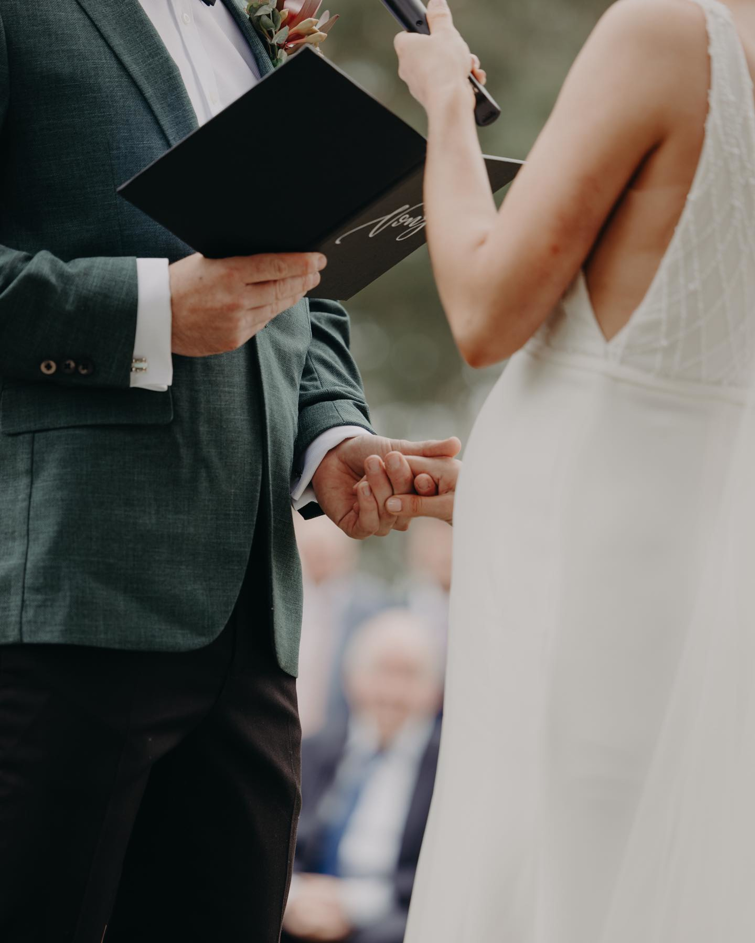 Close-up of a couple holding hands while exchanging wedding vows during an outdoor ceremony.