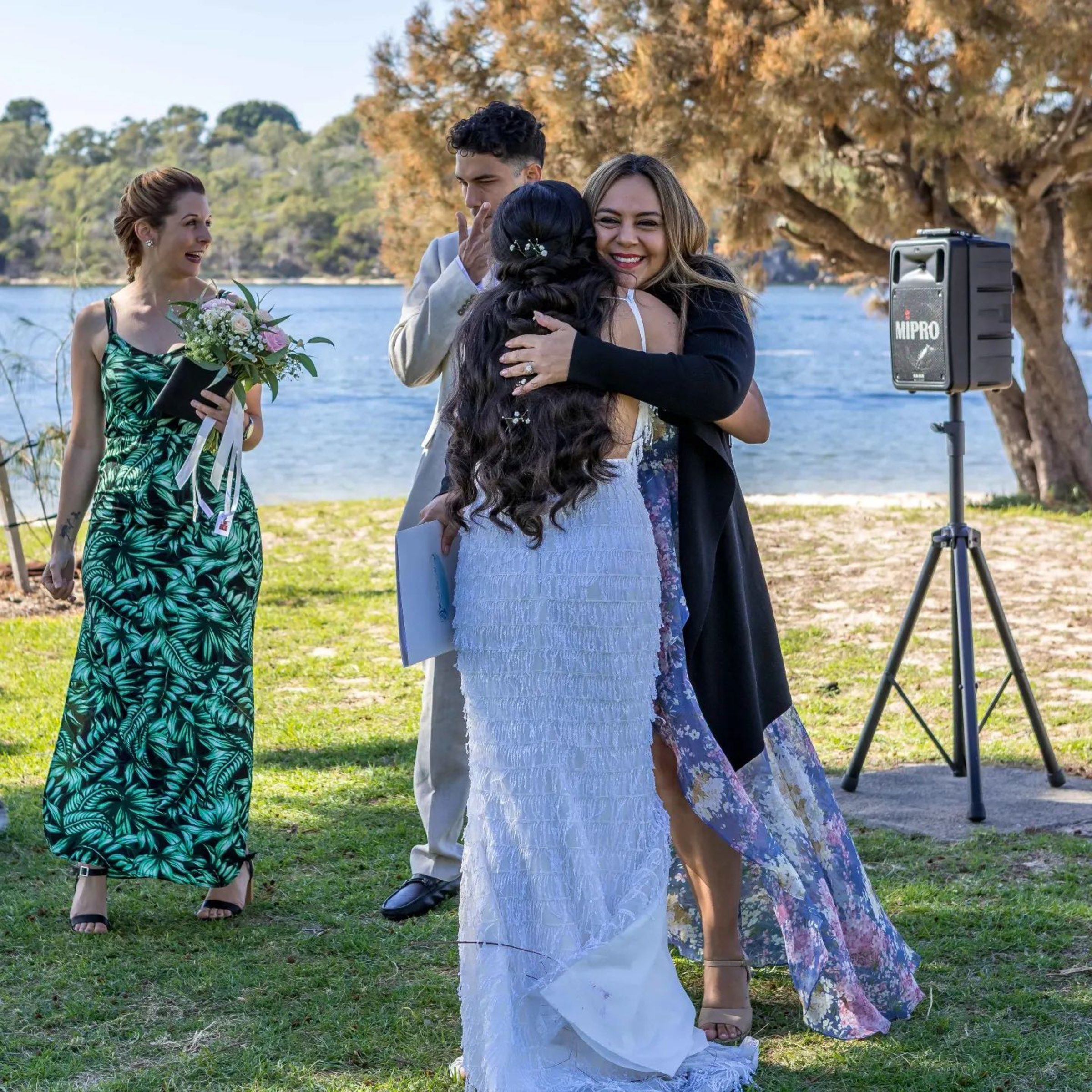 Guests warmly hug the bride during an outdoor lakeside wedding ceremony.
