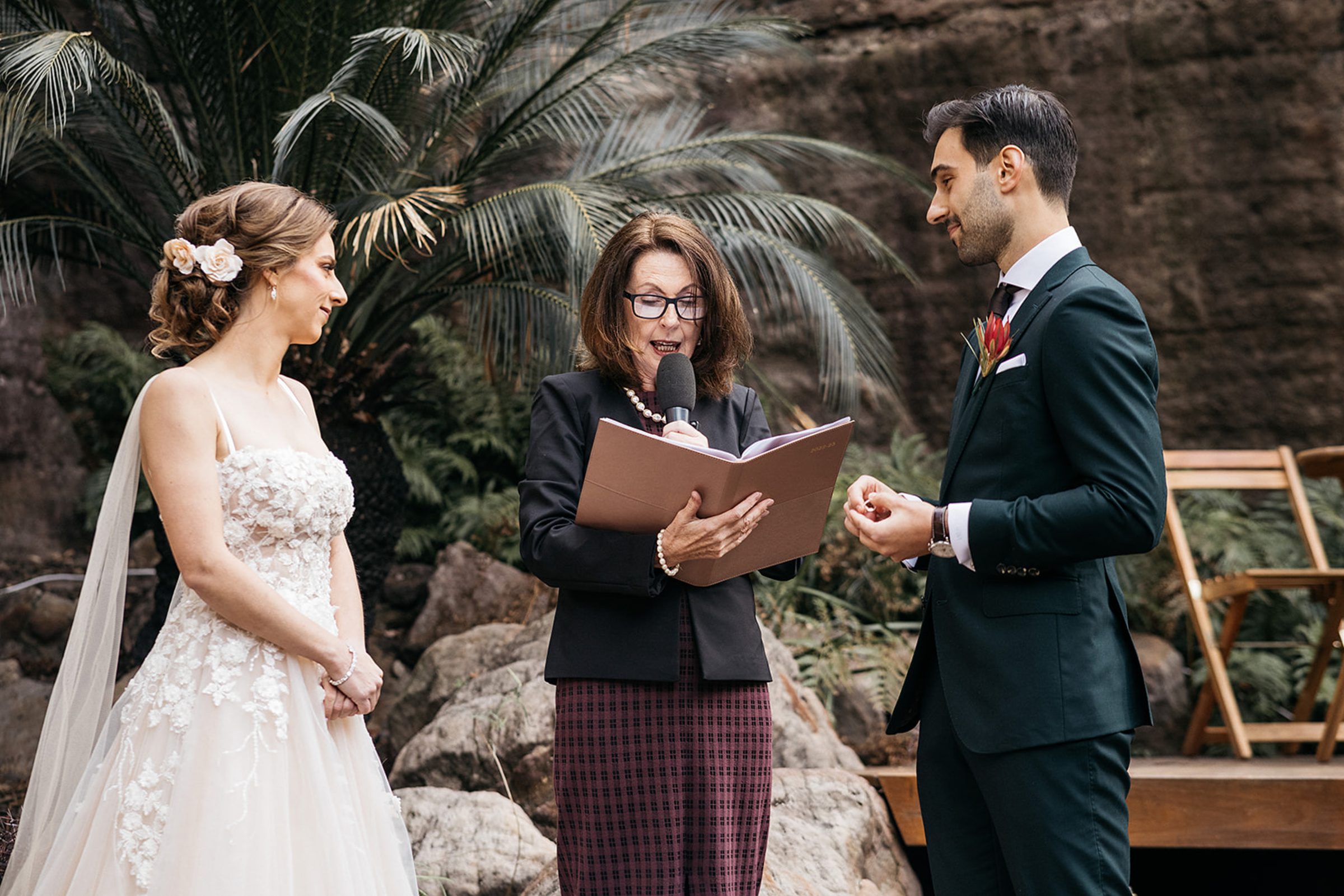 Bride and groom exchange vows with a celebrant during an outdoor garden wedding ceremony.