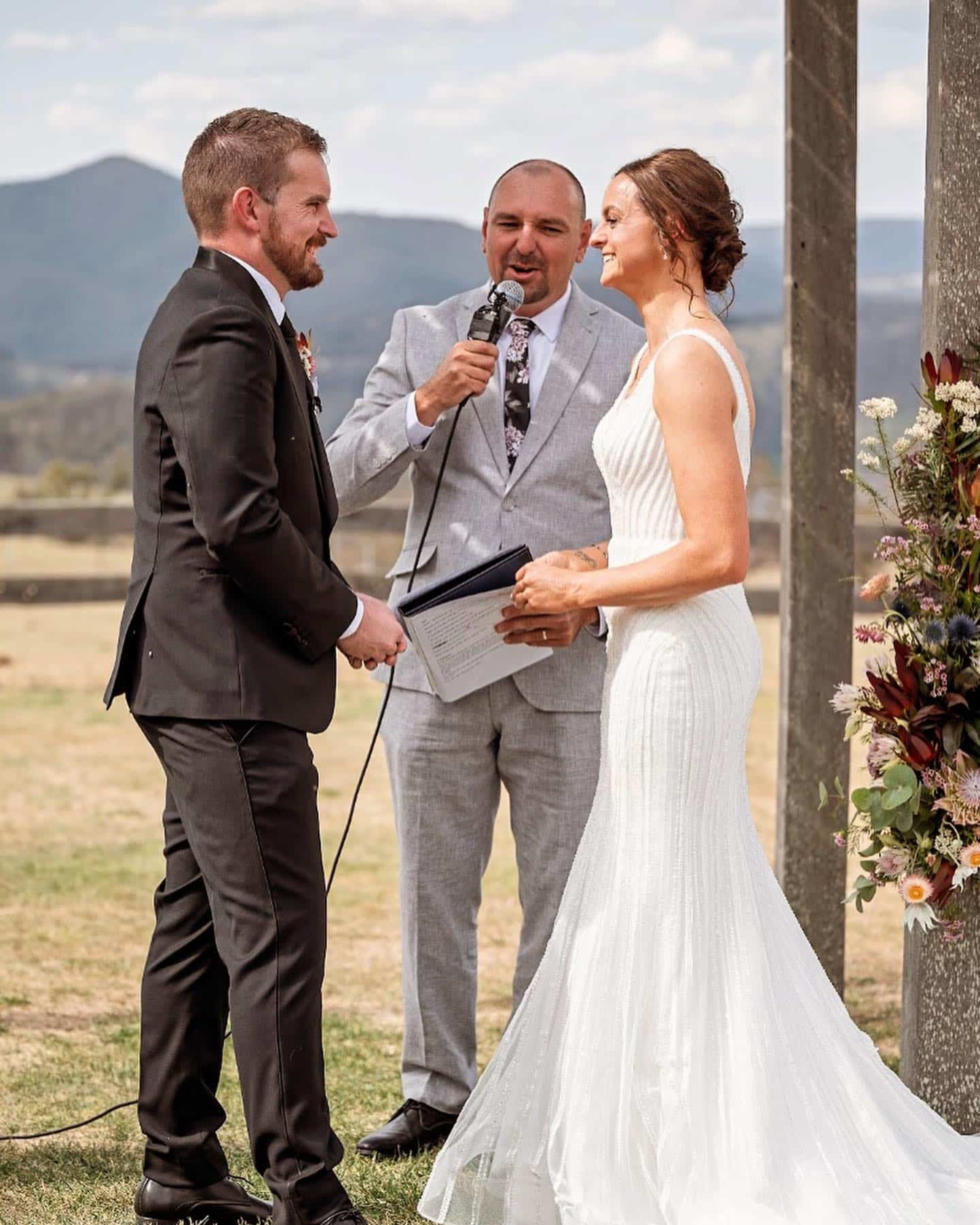 Couple exchanging vows outdoors with a celebrant in front of a mountain backdrop.