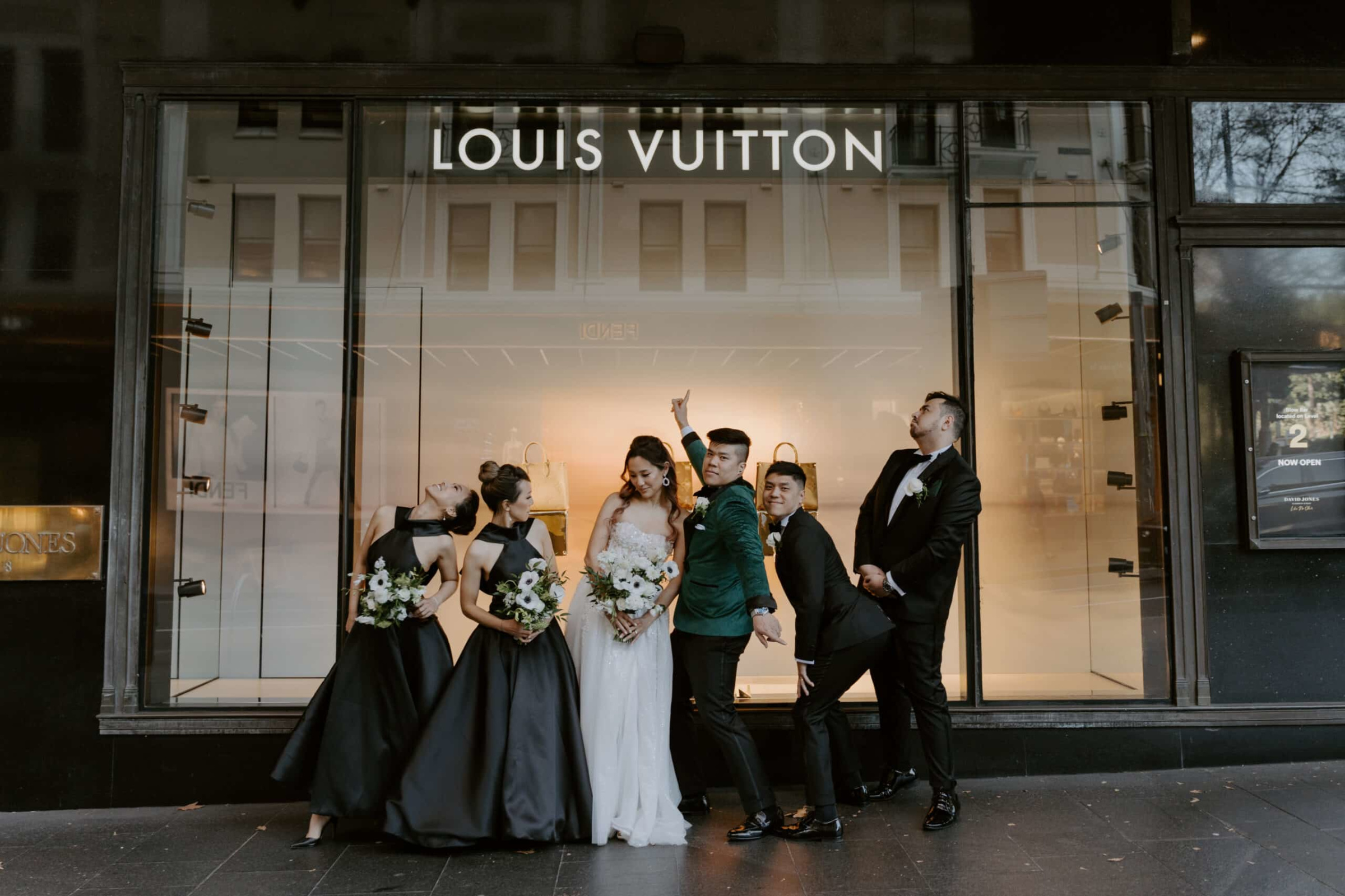 Playful wedding party poses in front of a luxury storefront in an urban city setting.
