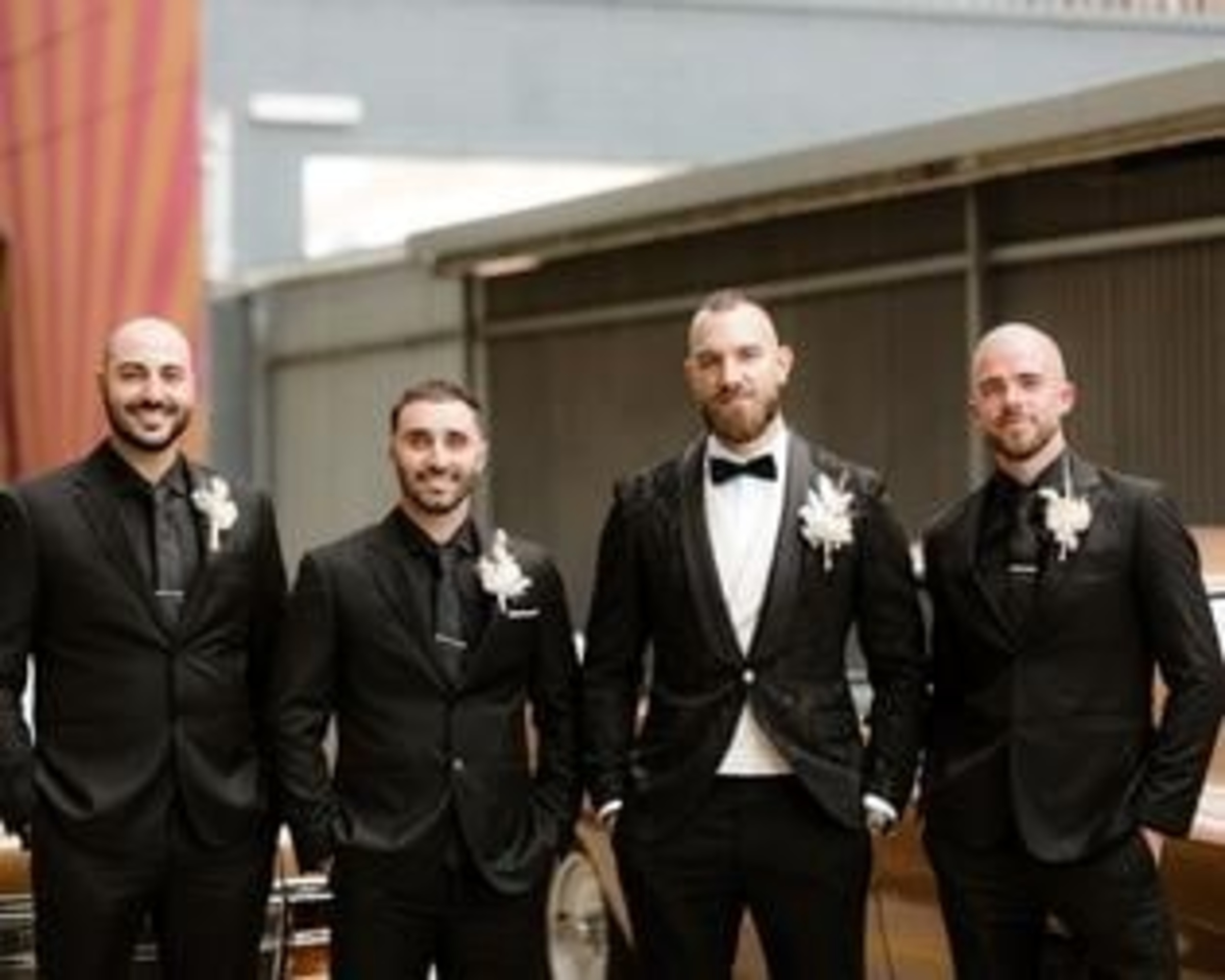 Groom and groomsmen in black suits with white boutonnieres posing in front of a vintage car.