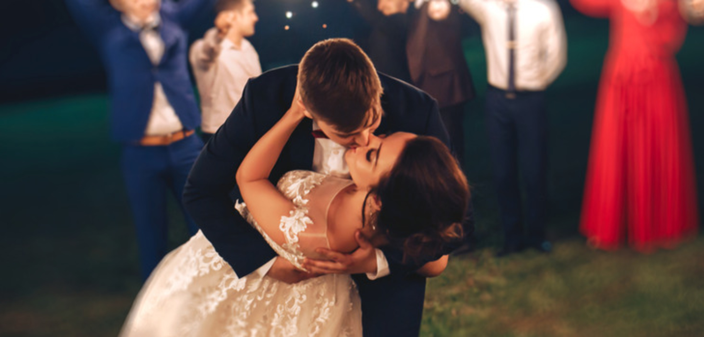 Bride and groom share a romantic dip and kiss at night surrounded by guests holding sparklers.
