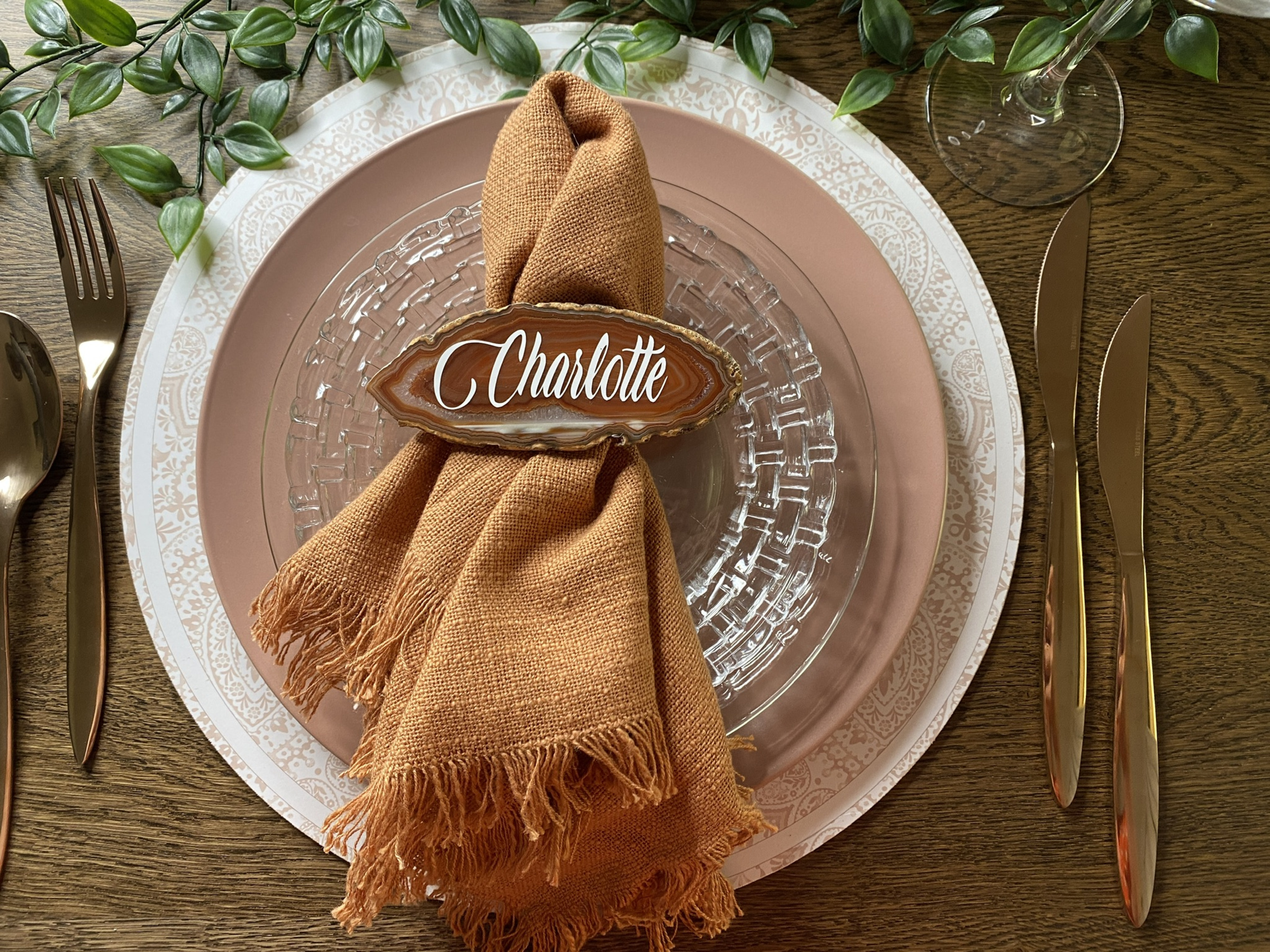 Rustic wedding place setting with personalized agate place card, terracotta napkin, and layered plates with greenery accents.