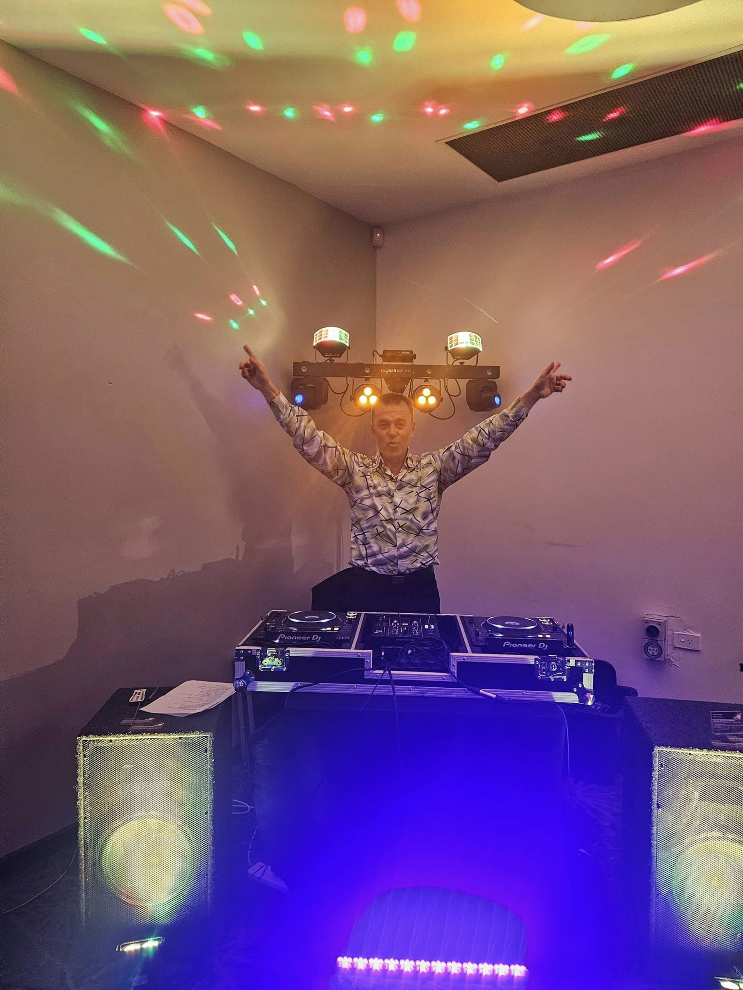 Wedding DJ performing behind a lit-up DJ booth with colorful disco lights filling the room.