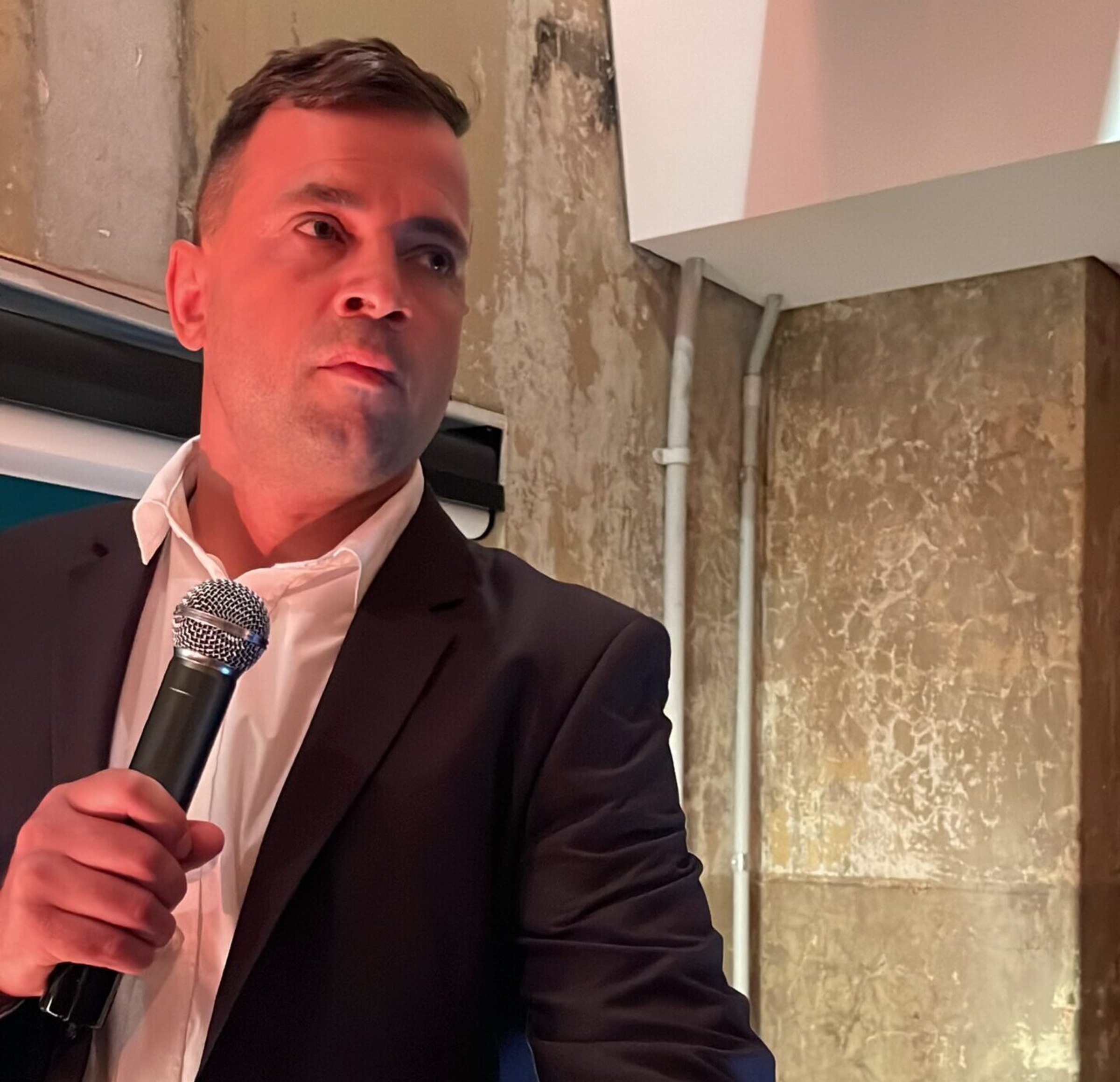 Wedding host in a suit holding a microphone and speaking indoors.