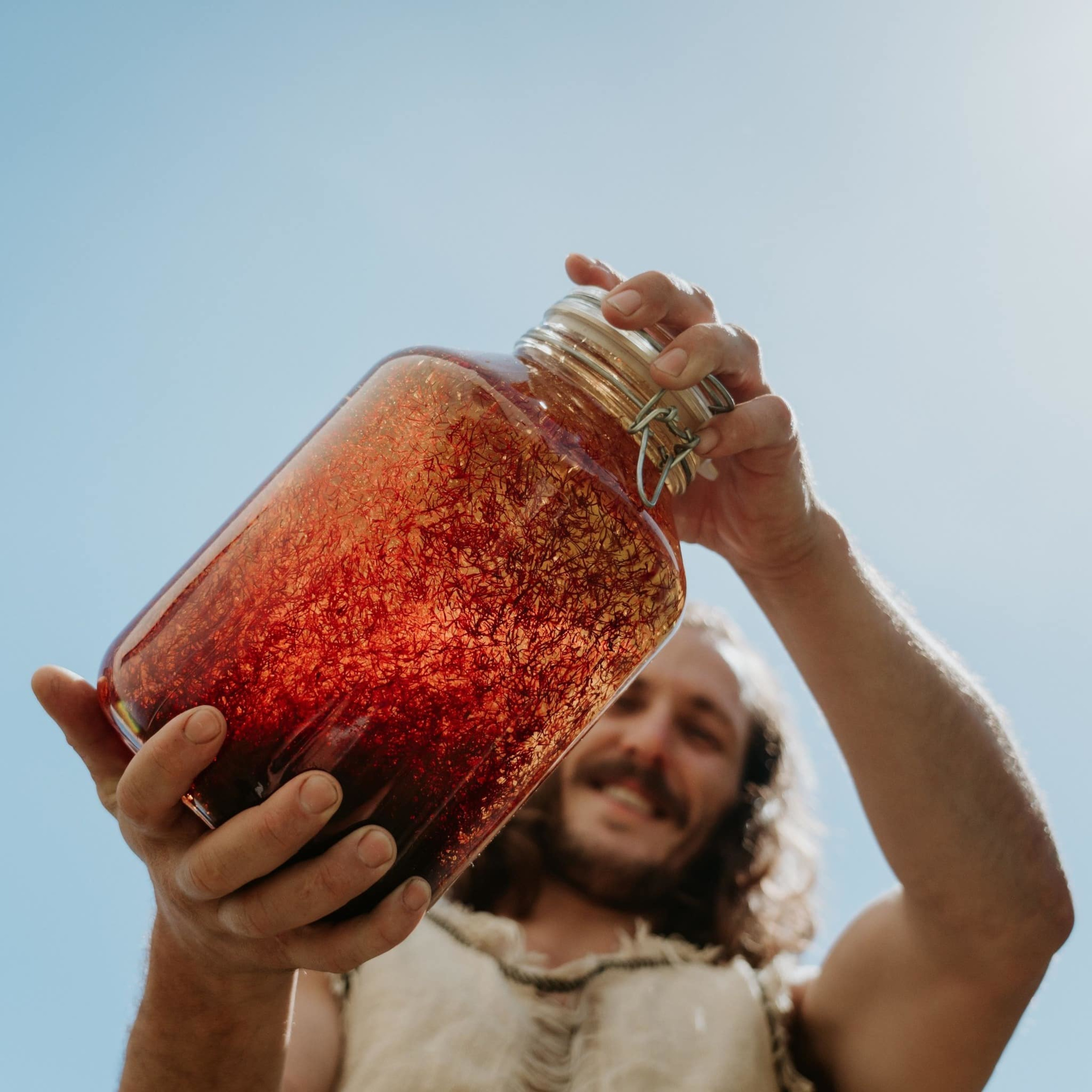 Person holding a large jar of red infused drink against a bright blue sky.