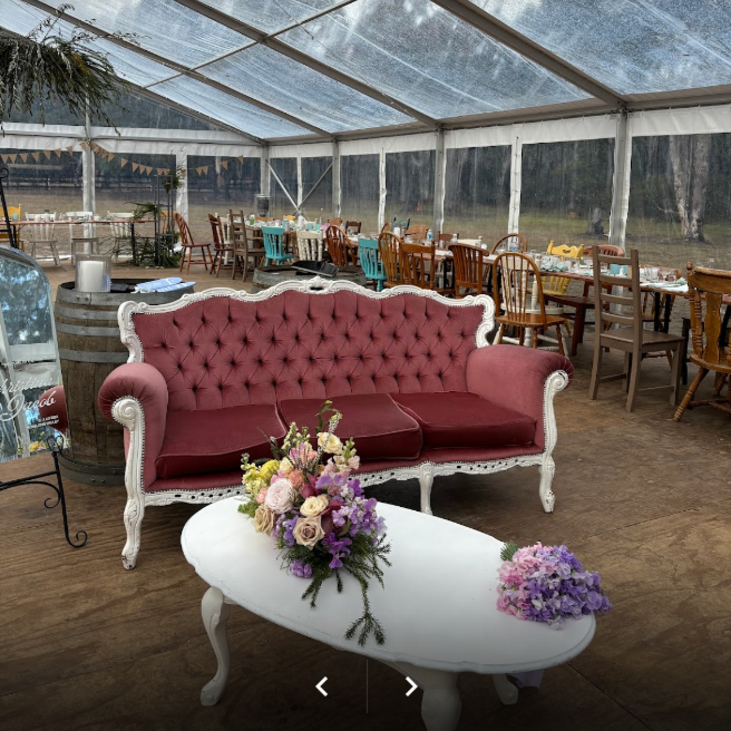 Vintage burgundy sofa and floral centerpiece in a clear marquee wedding reception setup.