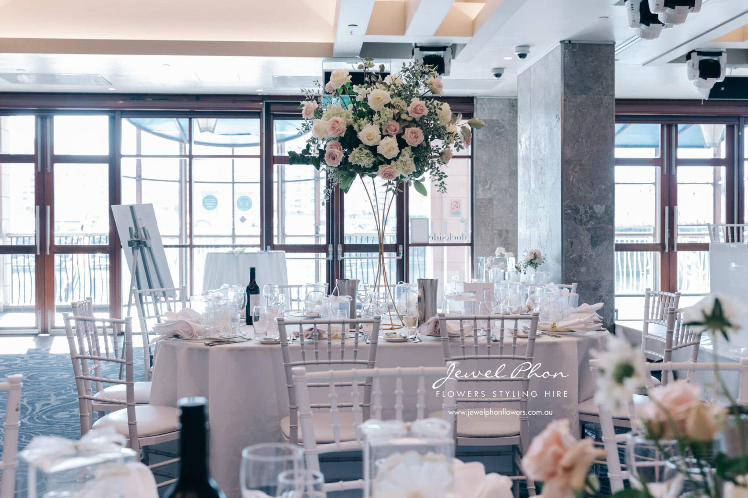 Elegant indoor wedding reception with tall blush and white floral centerpieces and white chair seating.