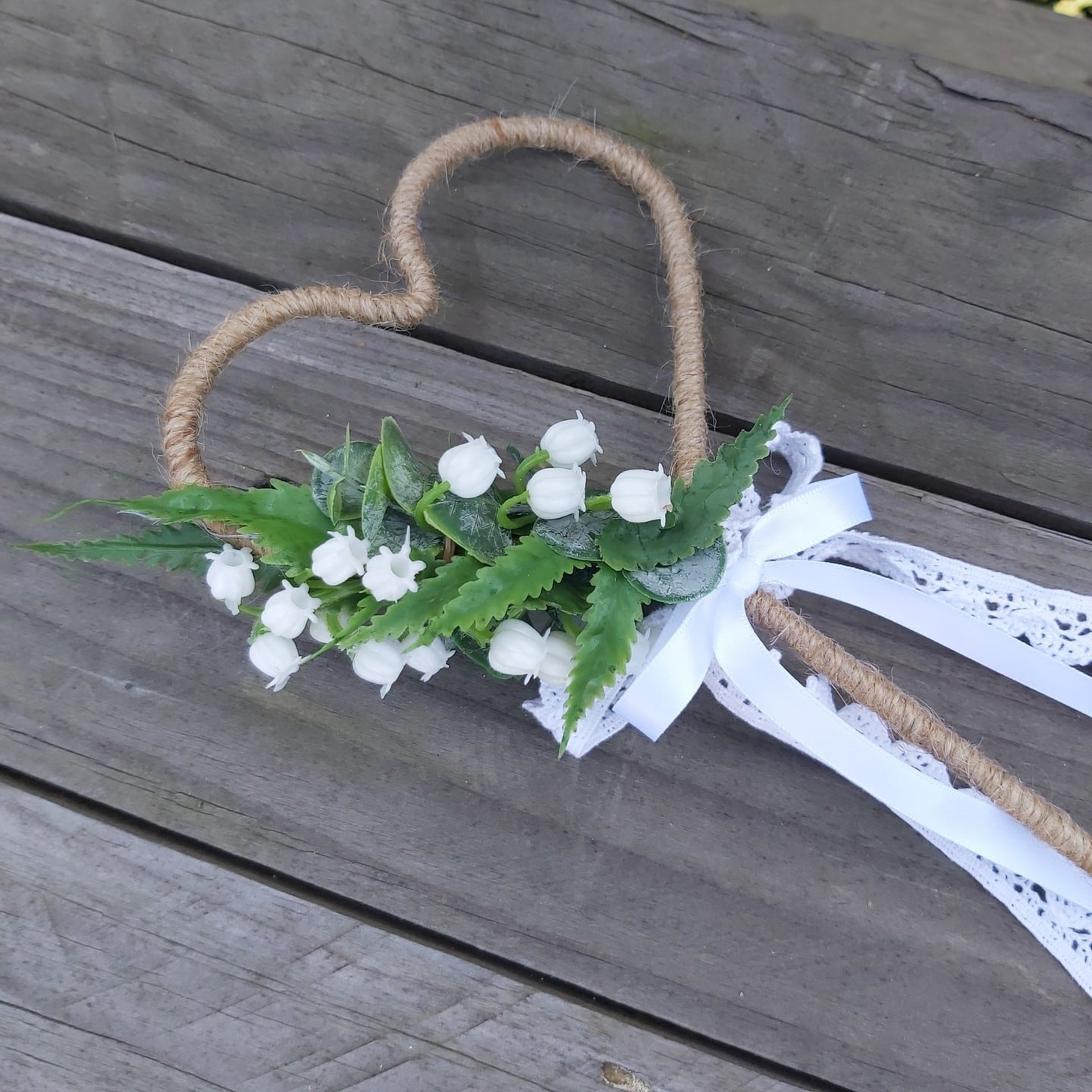 Rustic heart-shaped twine wedding wand with white flowers and lace ribbon on wooden boards
