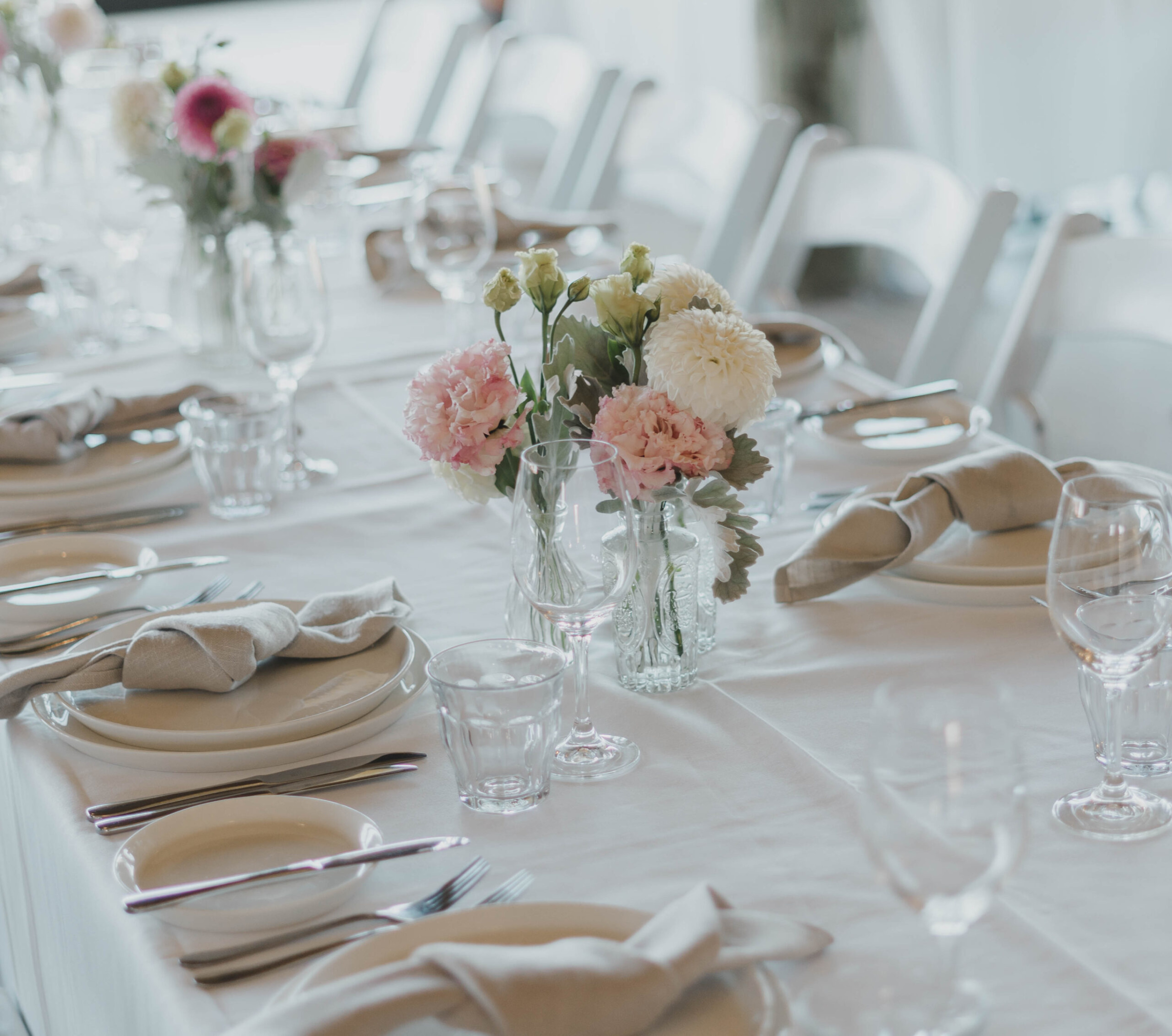Elegant wedding reception table with soft pink floral centerpieces and neutral napkins on white linens.