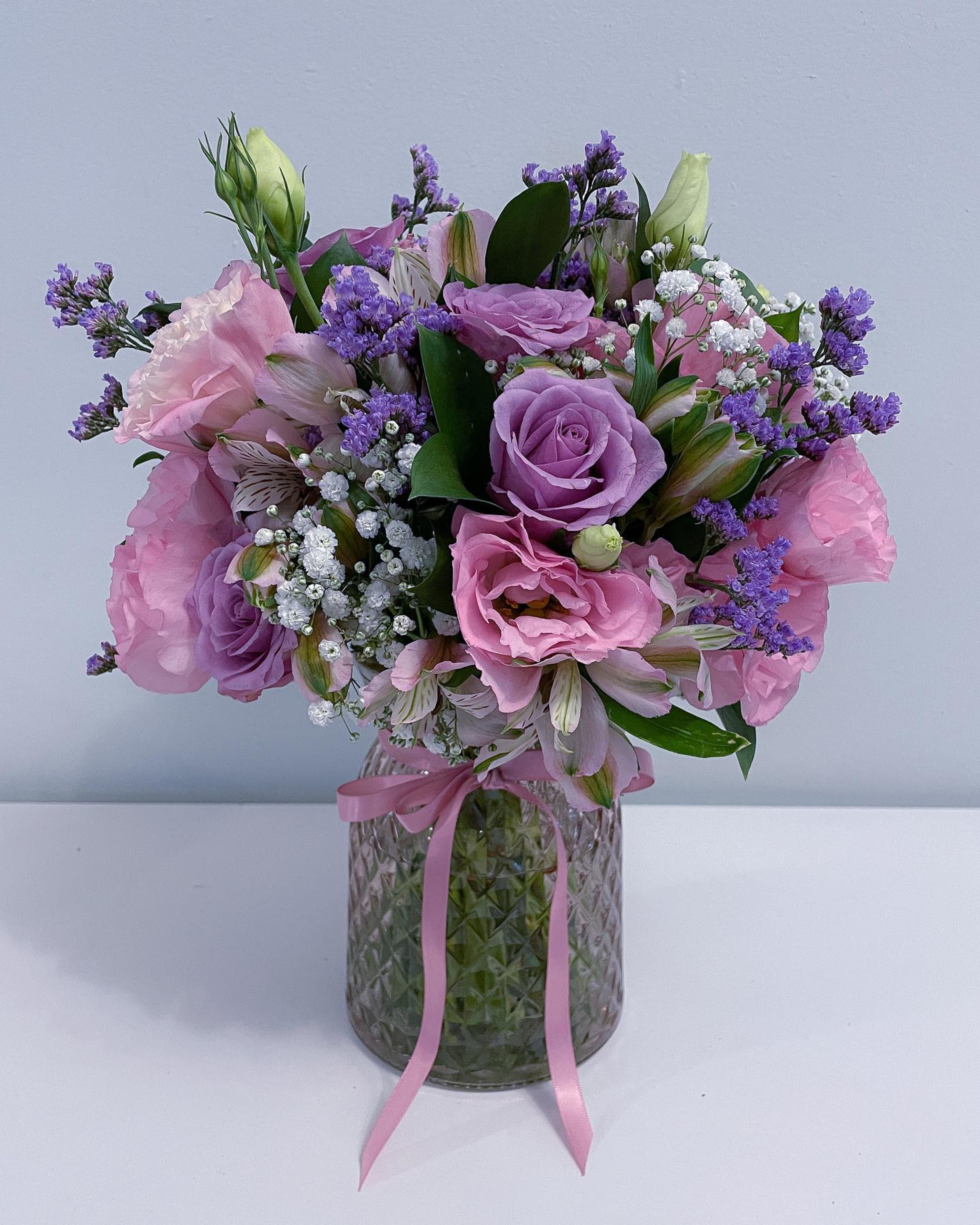 Romantic pink and purple floral arrangement in a glass vase tied with a pink ribbon.