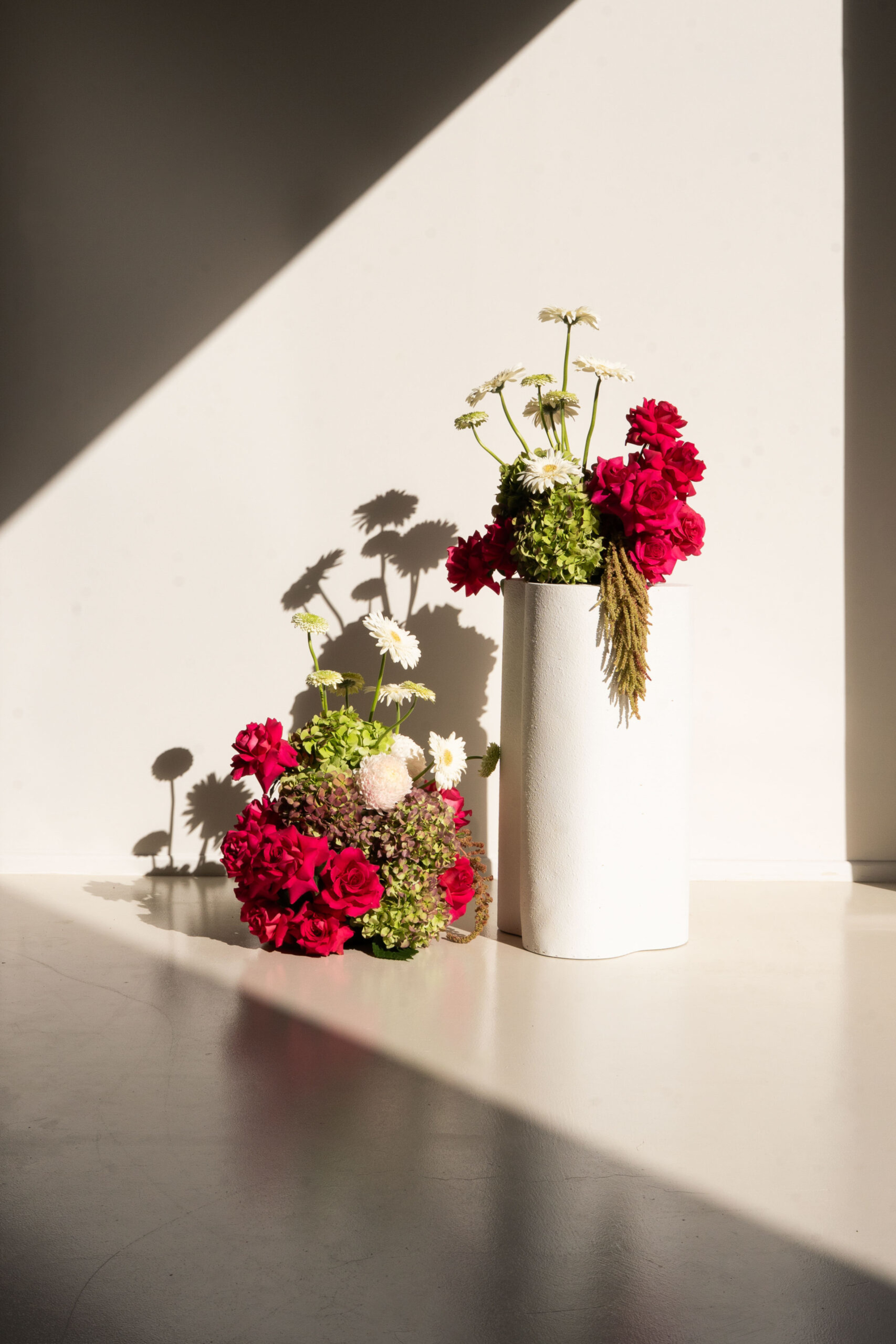 Modern white vase with bright pink and white floral arrangements in dramatic sunlight and shadow.