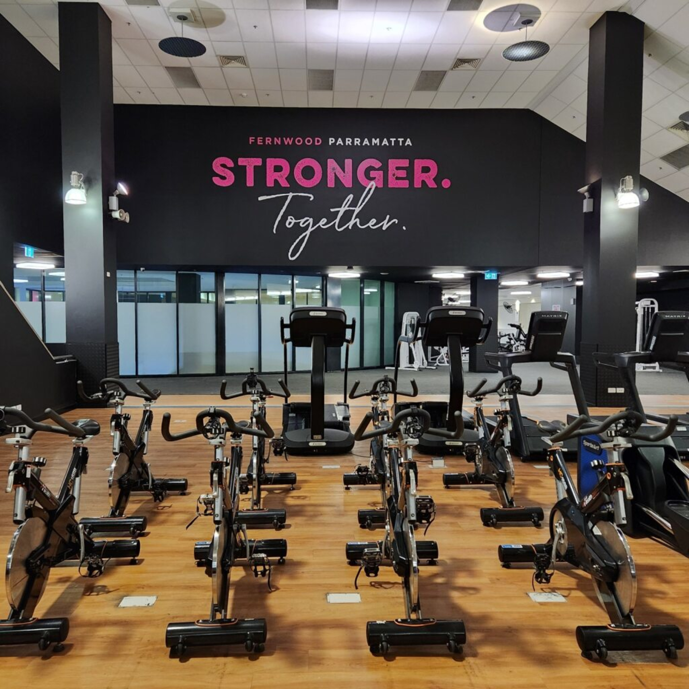 Modern indoor gym with rows of stationary bikes facing a wall sign that reads Stronger Together.