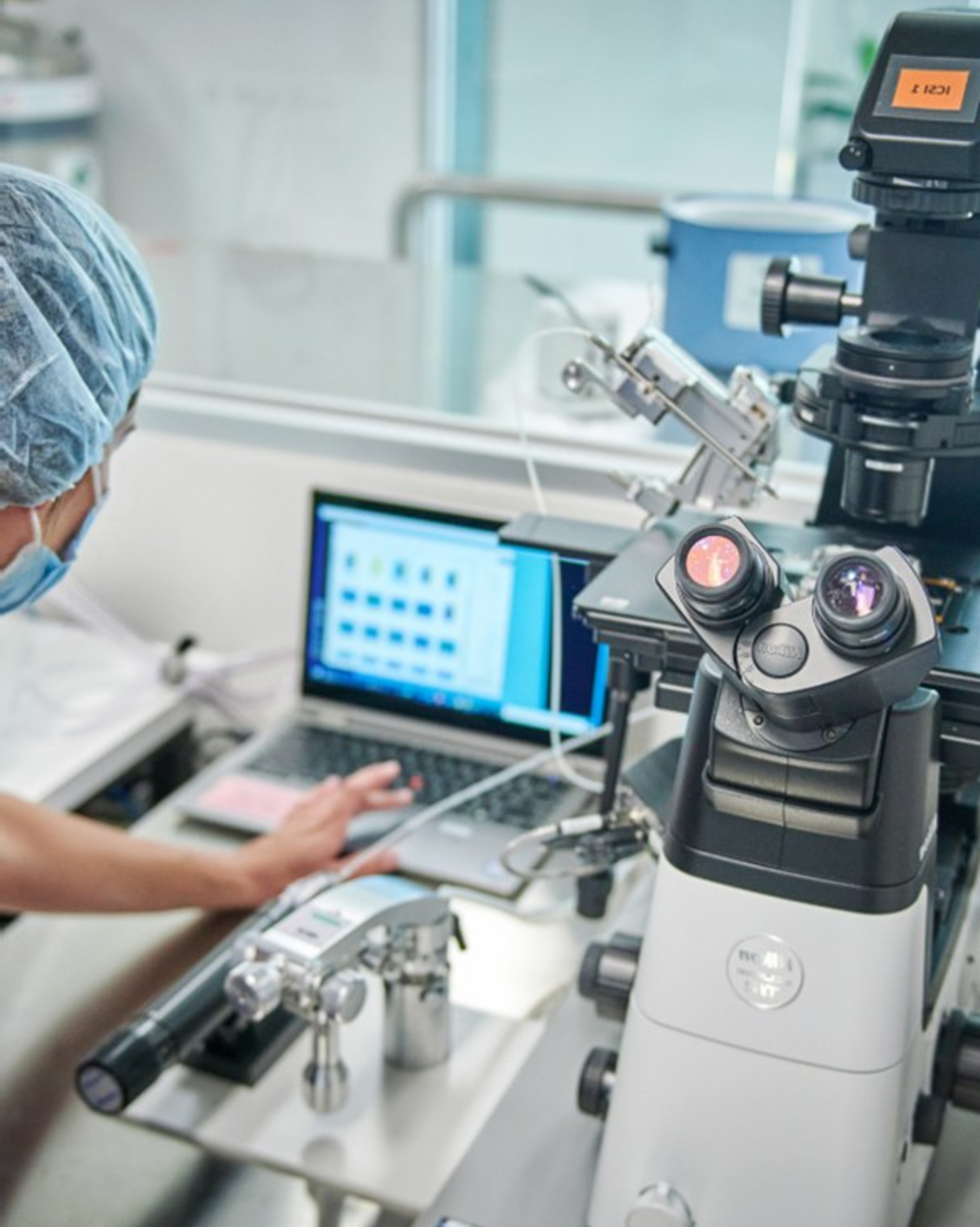 Scientist working at a computer beside an advanced microscope in a modern laboratory.